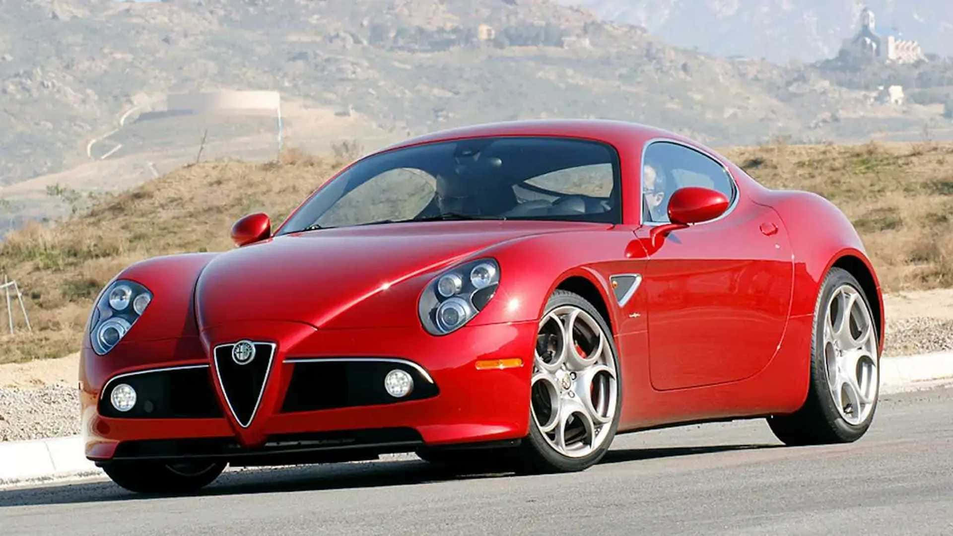 Alfa Romeo 8c Competizione 桌布 壁紙 — 一架亮麗的紅色愛快羅密歐跑車停泊在路邊，背景有乾燥的山丘和遠處的建築物。