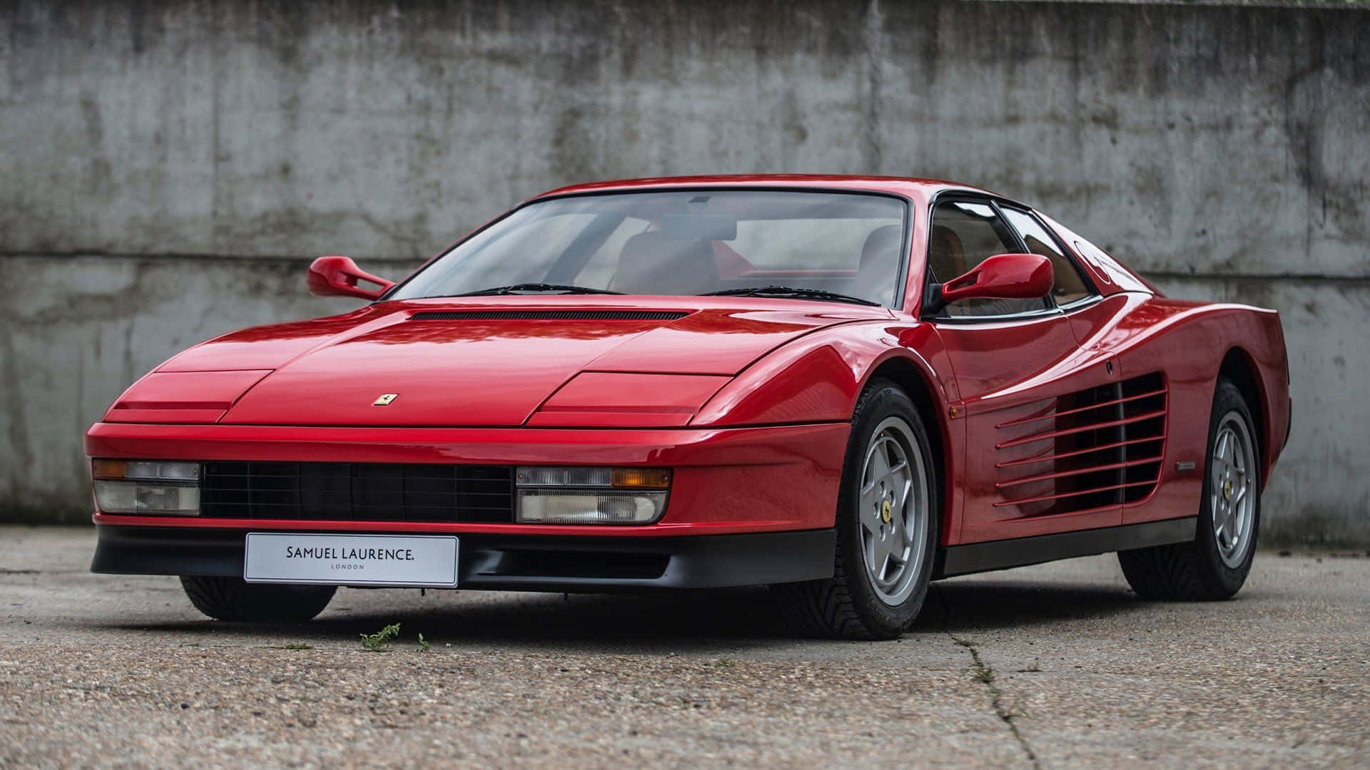 Ferrari Testarossa 桌布 壁紙 — 一架亮麗紅色法拉利Testarossa停泊在風化混凝土牆旁嘅碎石地面上。