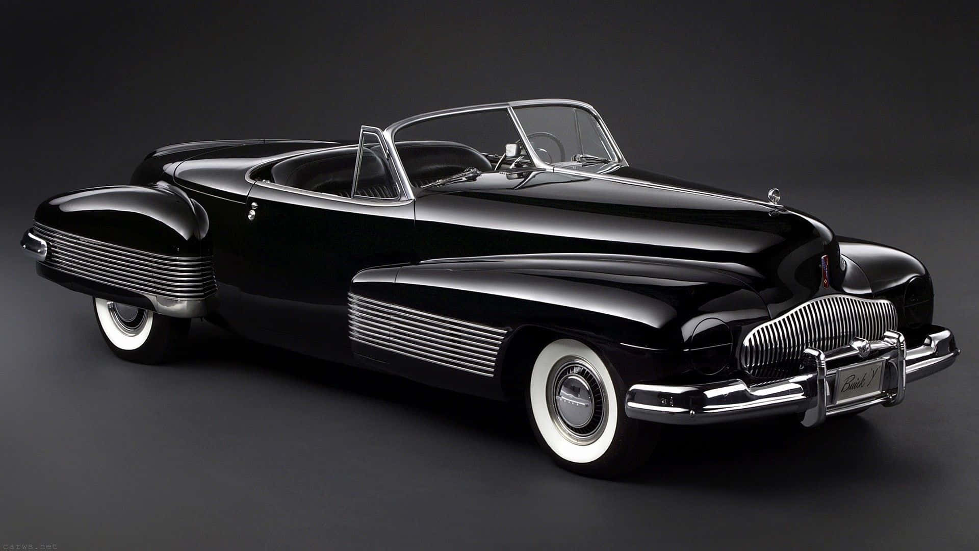 Black And White Vintage Car 桌布 壁紙 — 一架亮黑色1940年代敞篷車，帶有鍍鉻裝飾和白色側壁輪胎，在深色工作室背景前擺放。