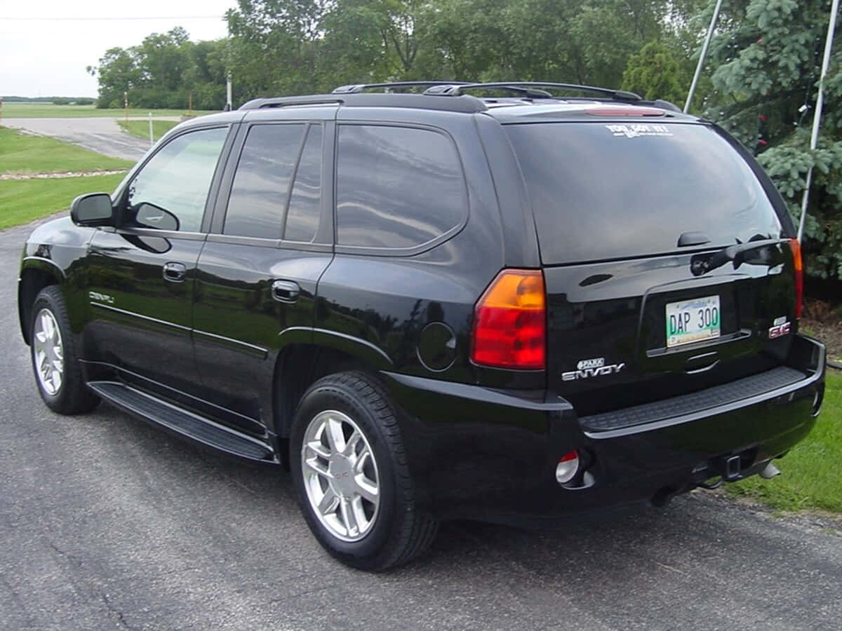 Gmc Envoy 桌布 壁紙 — 一架亮黑色GMC Envoy SUV停泊在瀝青路上，背景有樹木和草地。