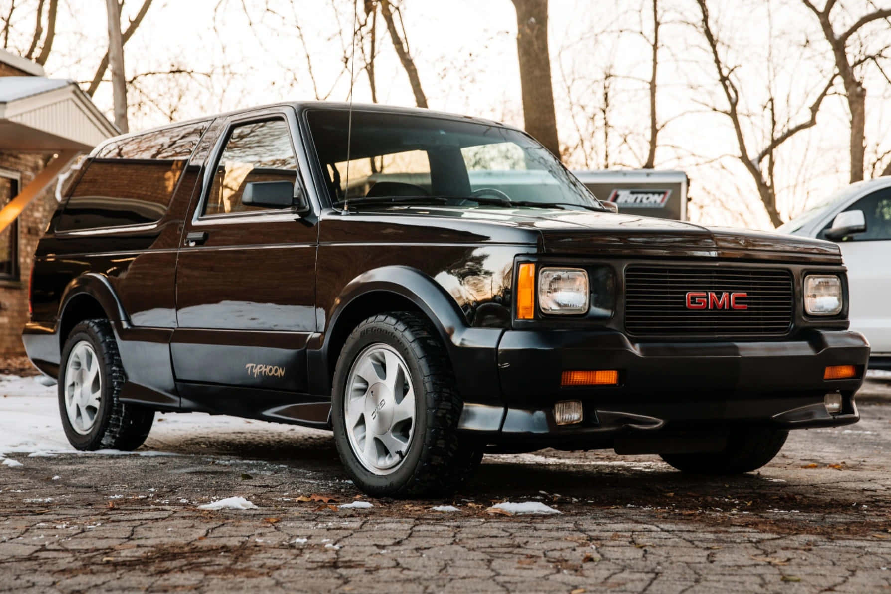 Gmc Typhoon 桌布 壁紙 — 一架亮黑色GMC Typhoon皮卡車停在白雪覆蓋的鵝卵石車道上，背景是光禿禿的樹木。