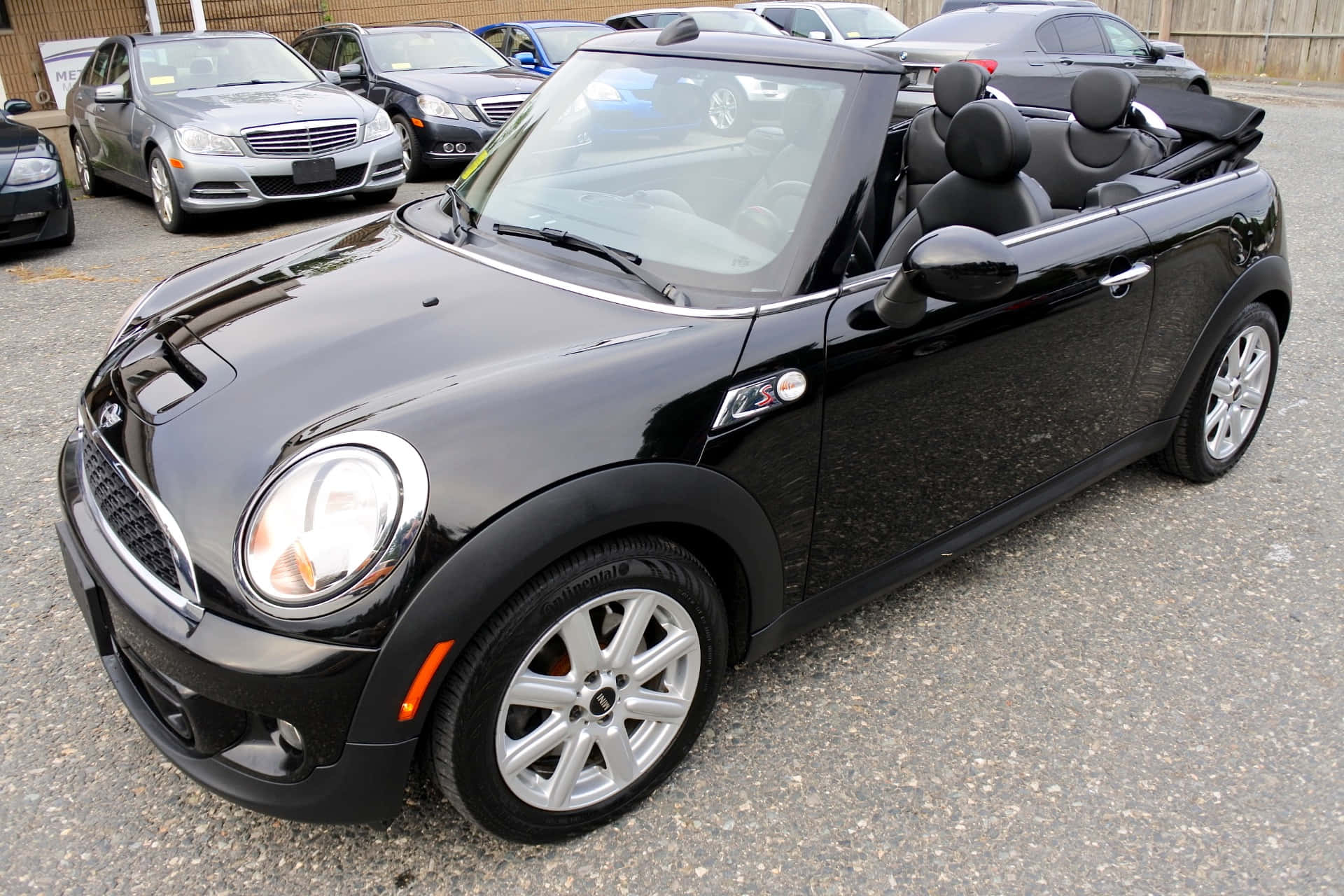Mini Cooper S Convertible 桌布 壁紙 — 一架亮黑色嘅Mini Cooper開篷車停泊喺碎石停車場，背景有其他車輛。