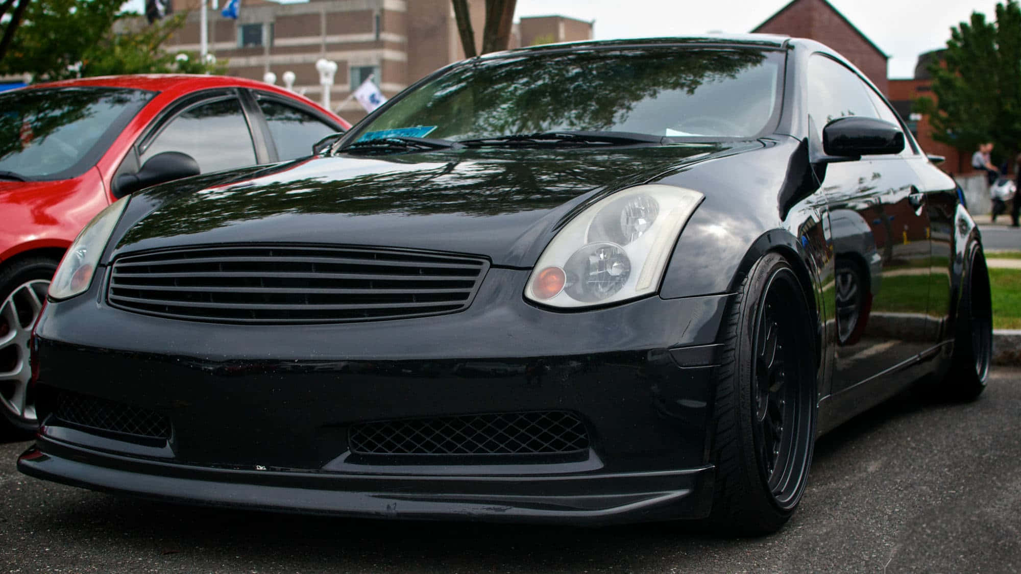 Infiniti G35 桌布 壁紙 — 一架亮黑色改裝運動轎跑車停泊在瀝青路上，旁邊有一輛紅色汽車，在日光下。