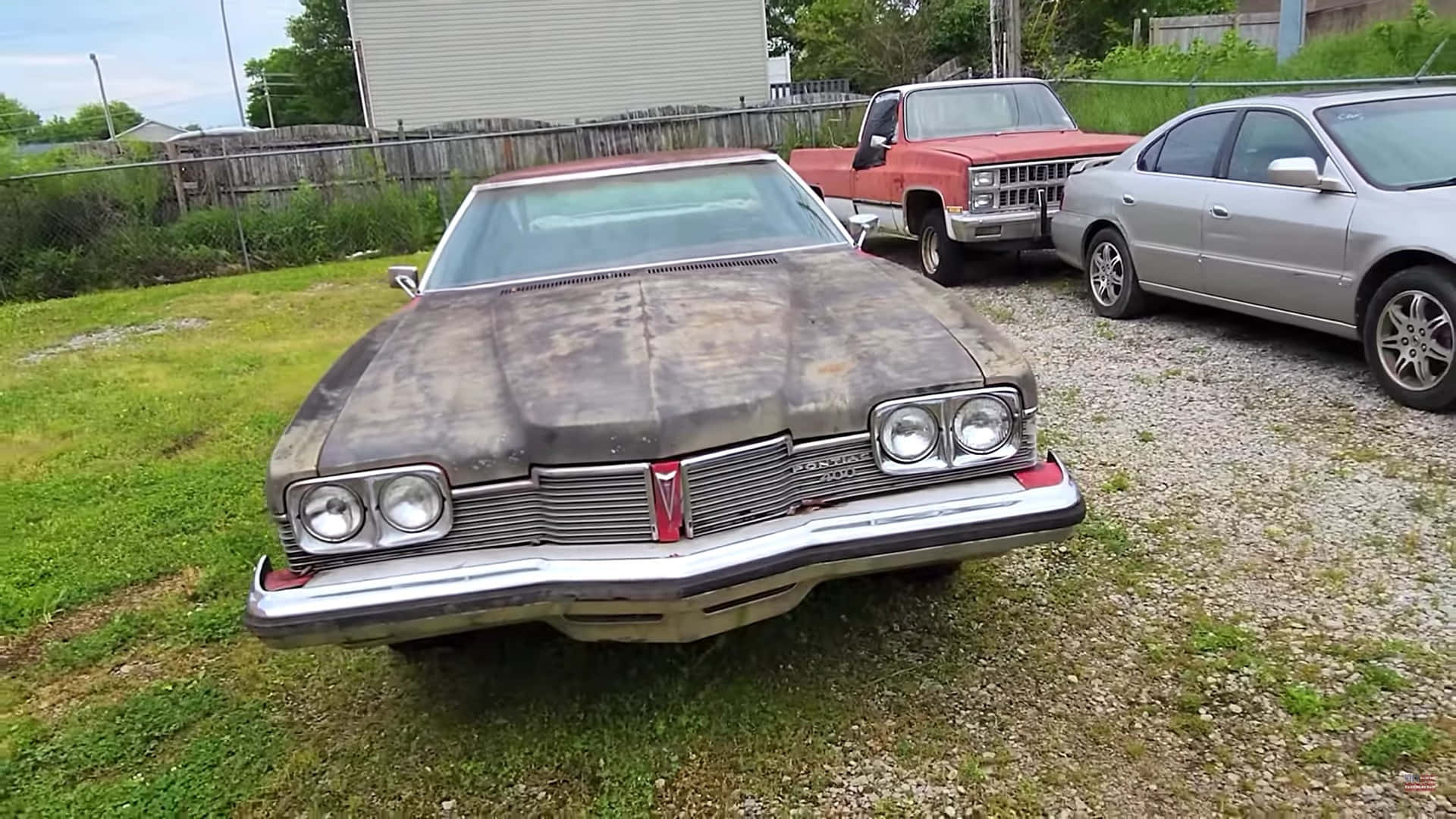 Pontiac Catalina 桌布 壁紙 — 一架佈滿灰塵的經典龐蒂亞克 Grand Prix 被遺棄在草地上，旁邊有一輛紅色 pickup 和一輛銀色轎車，天空多雲。
