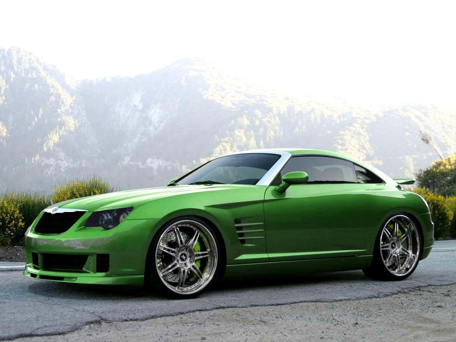 Chrysler Crossfire 桌布 壁紙 — 一架充滿活力的綠色跑車，配備定制鍍鉻輪圈，停泊在背景有森林覆蓋山丘的山路上。