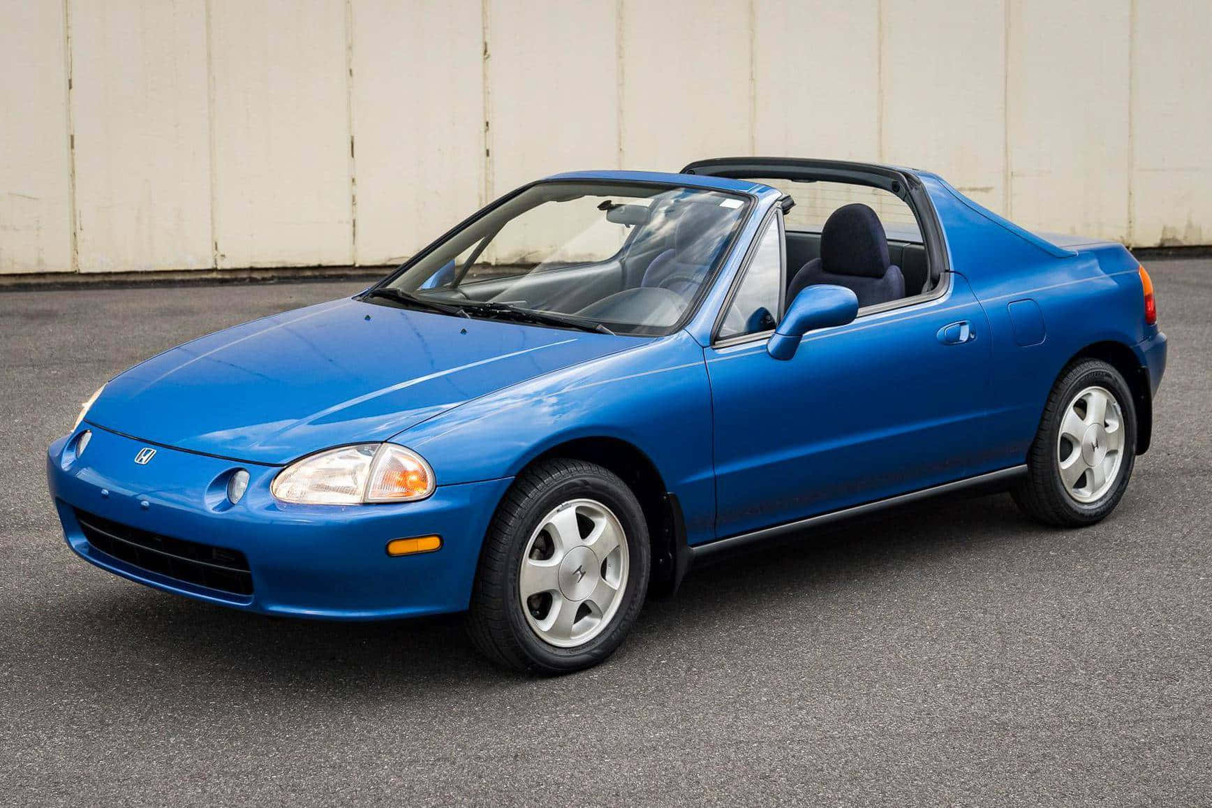 Honda Civic Del Sol 桌布 壁紙 — 一架充滿活力的藍色本田Del Sol開篷車停在瀝青路上，後面是一幅純米色牆壁。