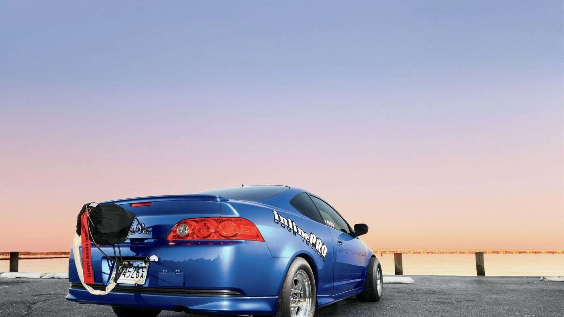 Rsx Type-s 桌布 壁紙 — 一架充滿活力的藍色跑車，帶有 'InlinePRO' 貼紙，停泊在日落時分的碼頭上，天空呈現漸變色。