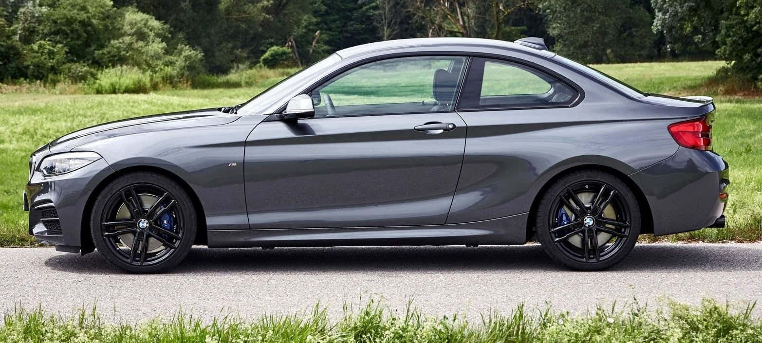 Bmw 2 Series 桌布 壁紙 — 一架光滑的啞光灰色寶馬雙門轎跑車停泊在碎石路上，旁邊是充滿活力的綠草和樹木。