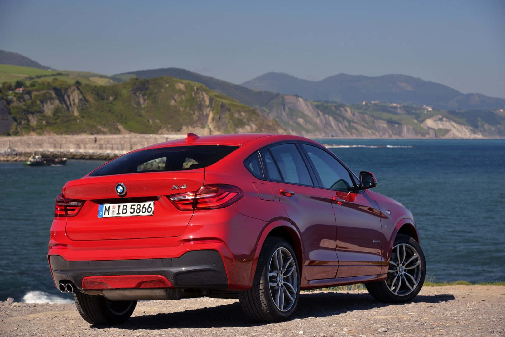 Bmw X4 桌布 壁紙 — 一架光澤的紅色BMW X4 SUV停泊在海岸懸崖上，俯瞰深藍色的大海，背景是綠色的山丘。