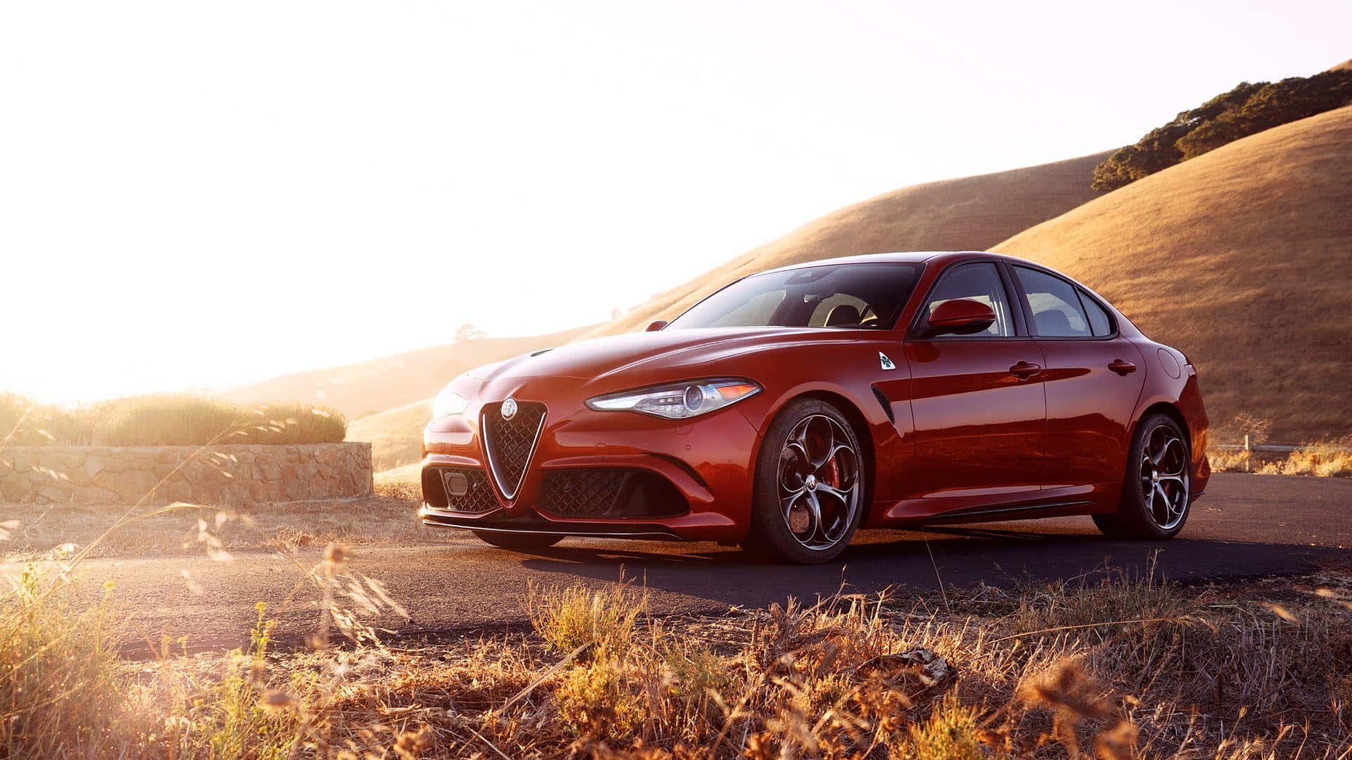 Alfa Romeo Giulia 桌布 壁紙 — 一架光澤的紅色愛快羅密歐房車停泊在蜿蜒的道路上，正值黃金時刻，背景是起伏的山丘。