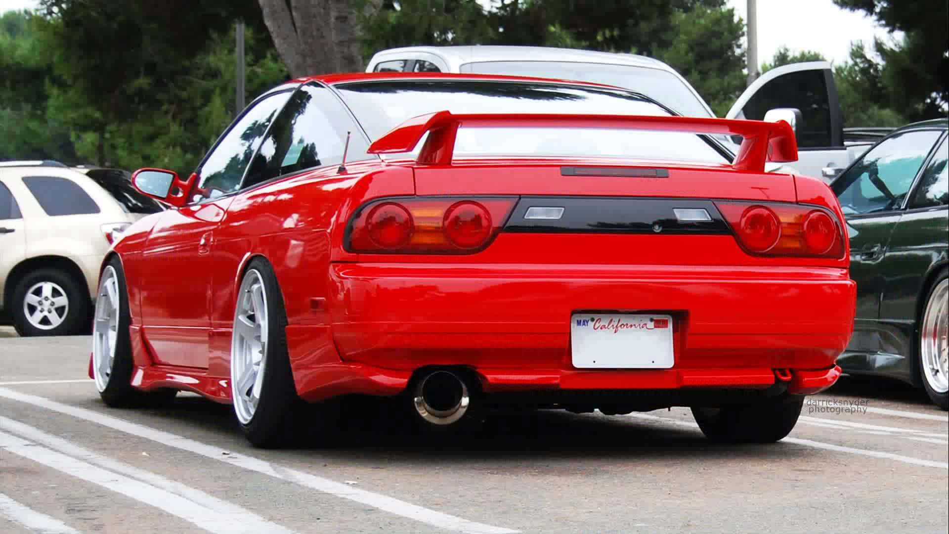 「Bold Style – Nissan 180sx」 壁紙 — 一架光澤的紅色日產Skyline R34跑車停泊在停車場，背景有樹木和其他車輛。