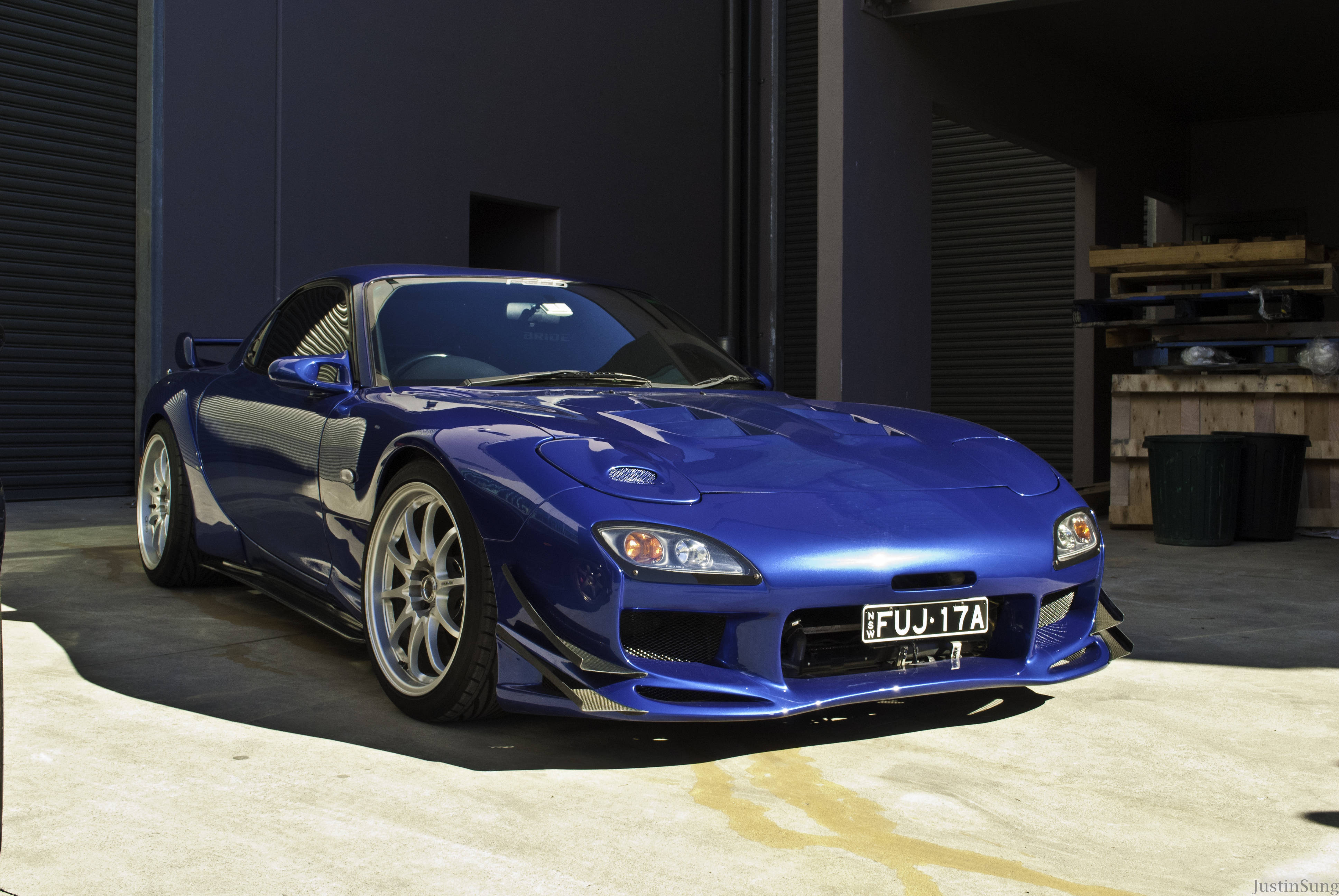 Mazda 桌布 壁紙 — 一架光澤藍色Mazda RX-7跑車停泊在車庫中，陽光在混凝土上投射出銳利的陰影。