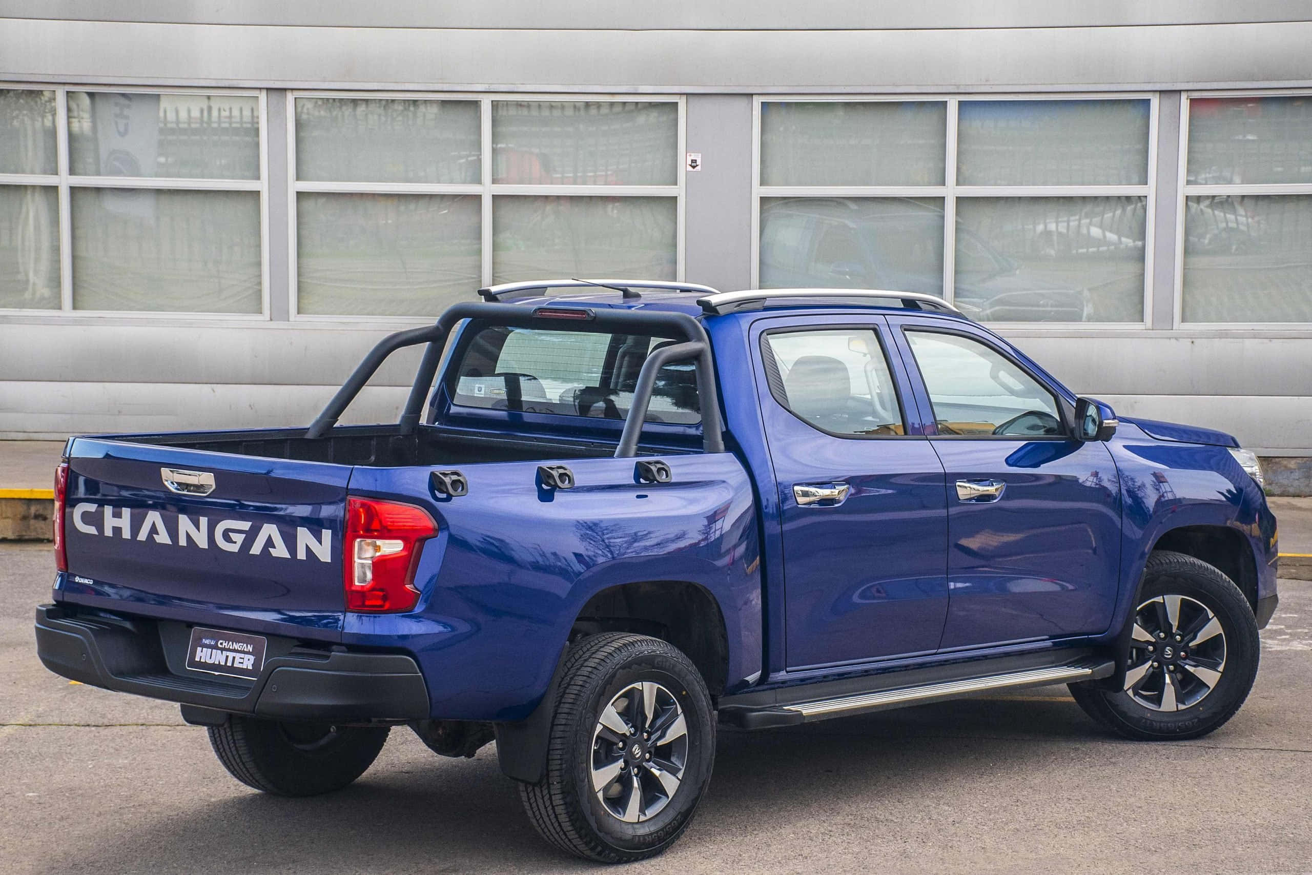 Changan 桌布 壁紙 — 一架光澤藍色長安獵手皮卡車停放在戶外，背景係一座現代建築。