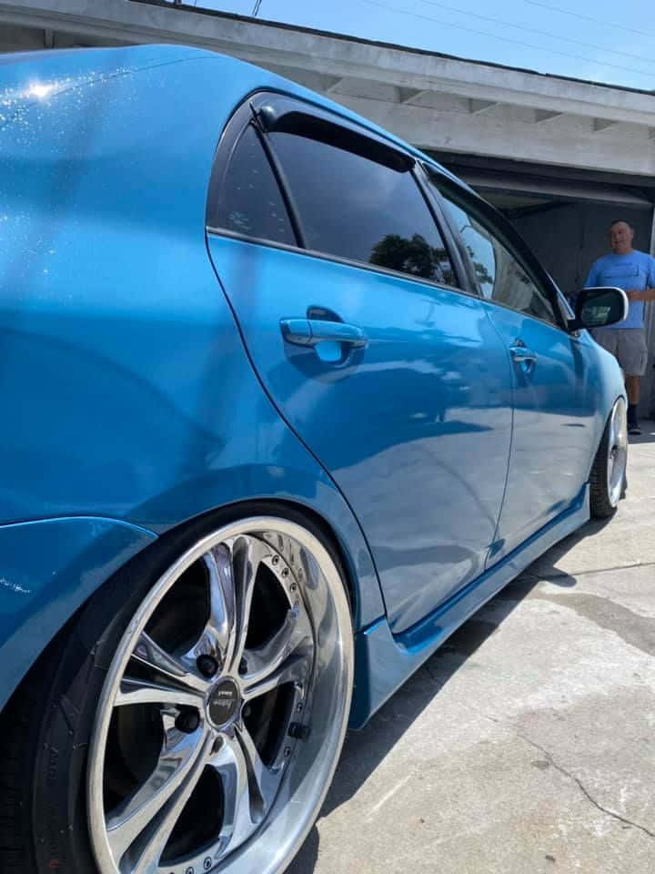 Azure Blue 桌布 壁紙 — 一架光面藍色改裝房車配備定制鍍鉻輪圈，停泊在混凝土高架橋下，附近站著一名男子。