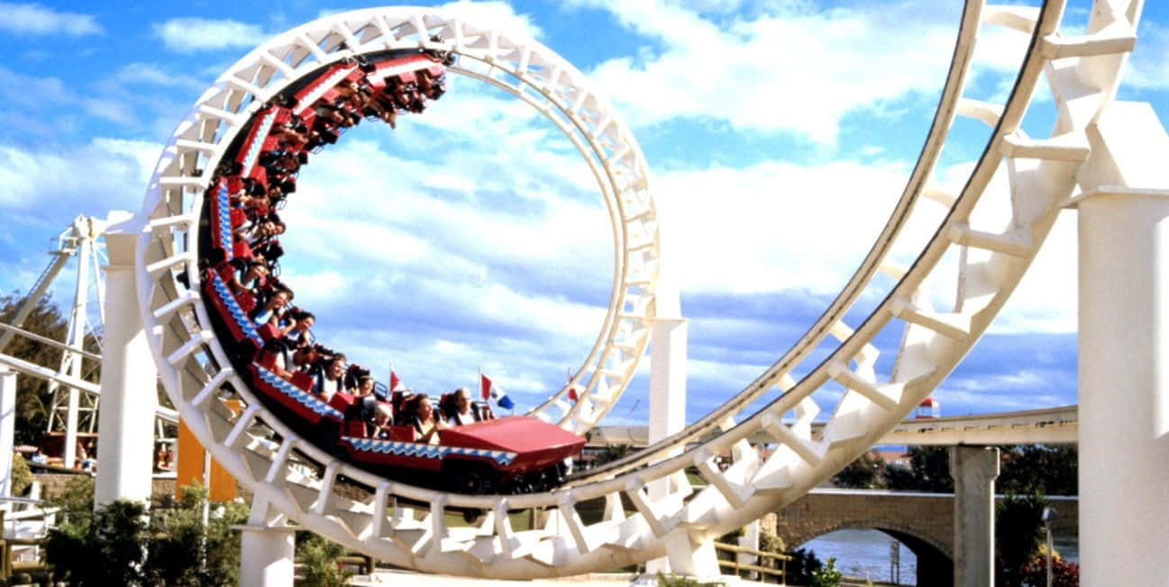 Roller Coaster 桌布 壁紙 — 一架刺激的紅色過山車載著乘客尖叫著穿過一個巨大的白色環圈，背景是晴朗的藍天和蓬鬆的白雲。
