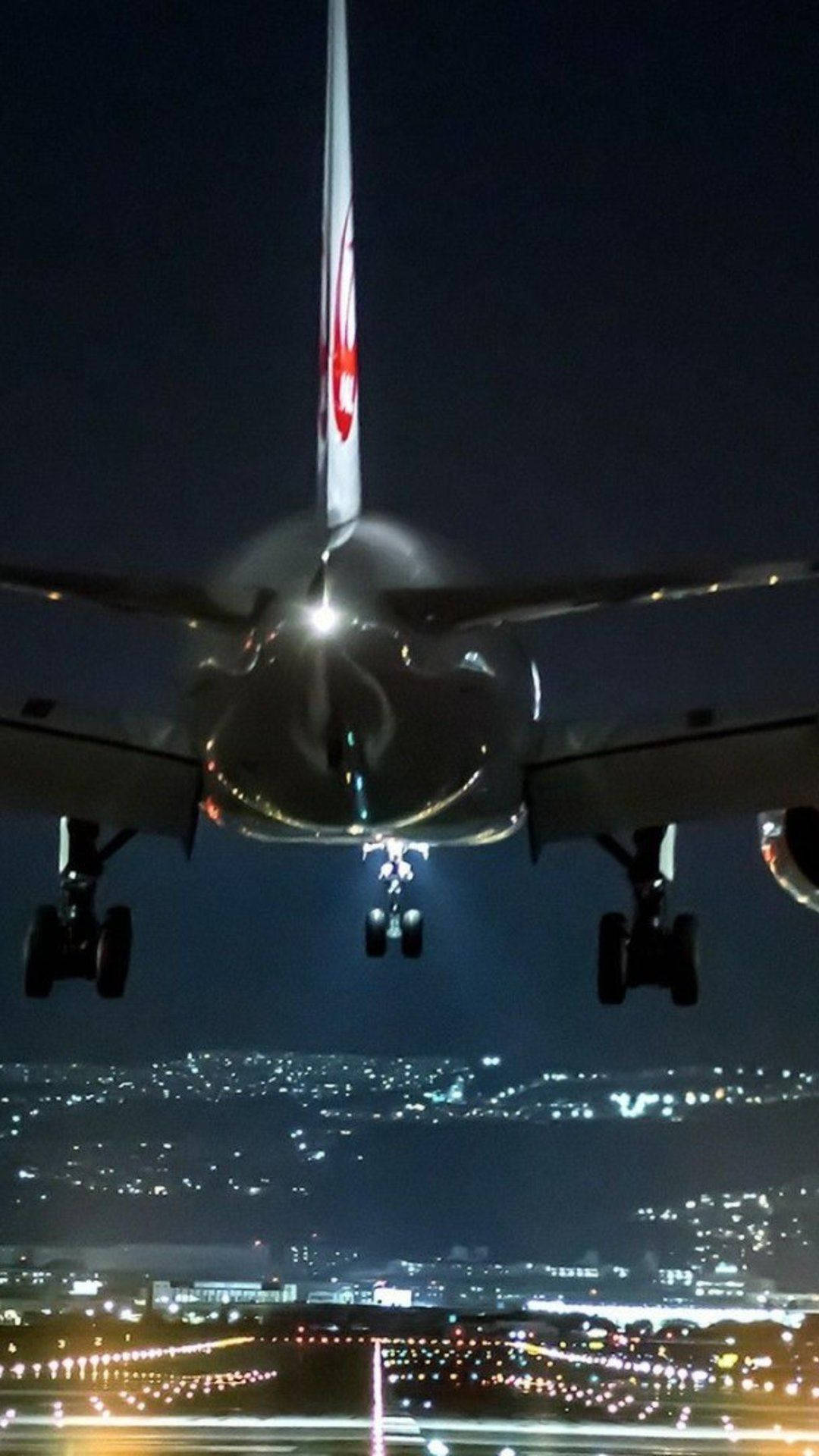 飛機 桌布 壁紙 — 一架商用飛機在夜間下降，降落燈亮起，背景是下方閃爍的城市燈光。