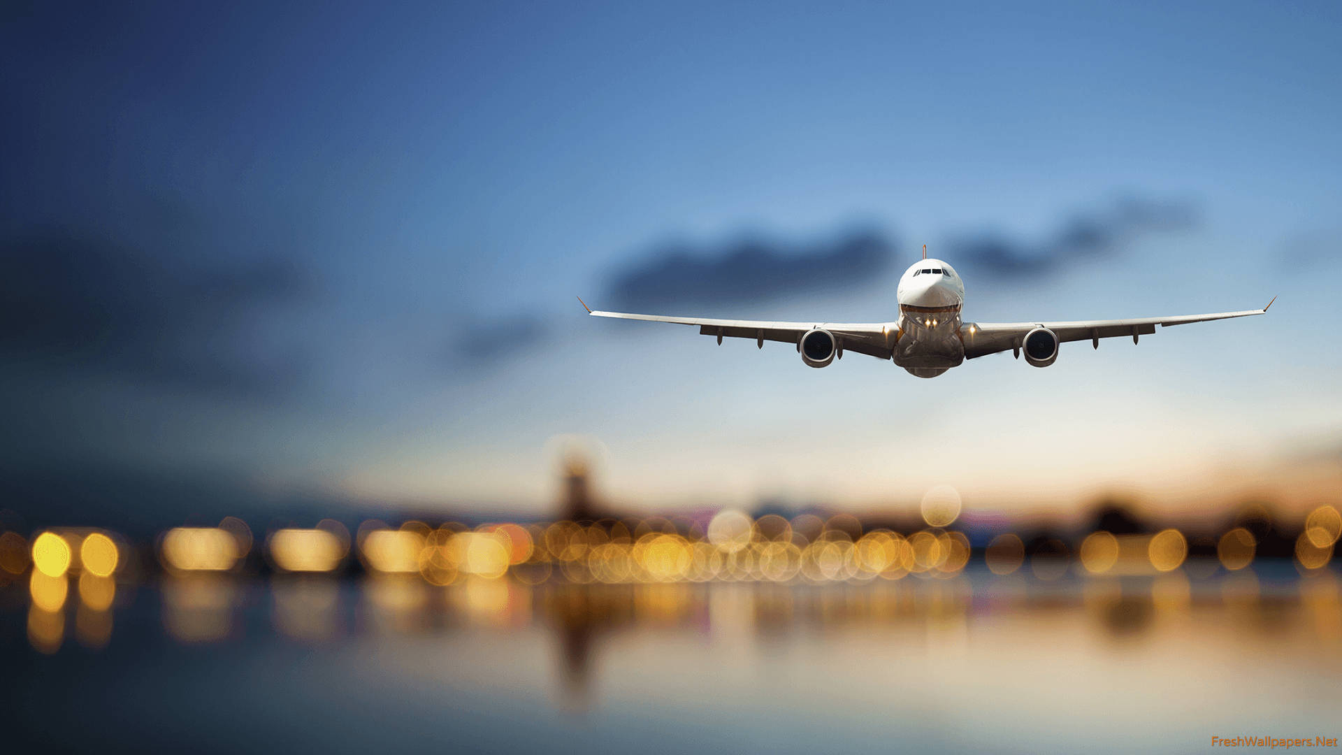 飛機 桌布 壁紙 — 一架商用飛機在暮色天空中飛過，下方模糊的城市燈光倒映在水面上。