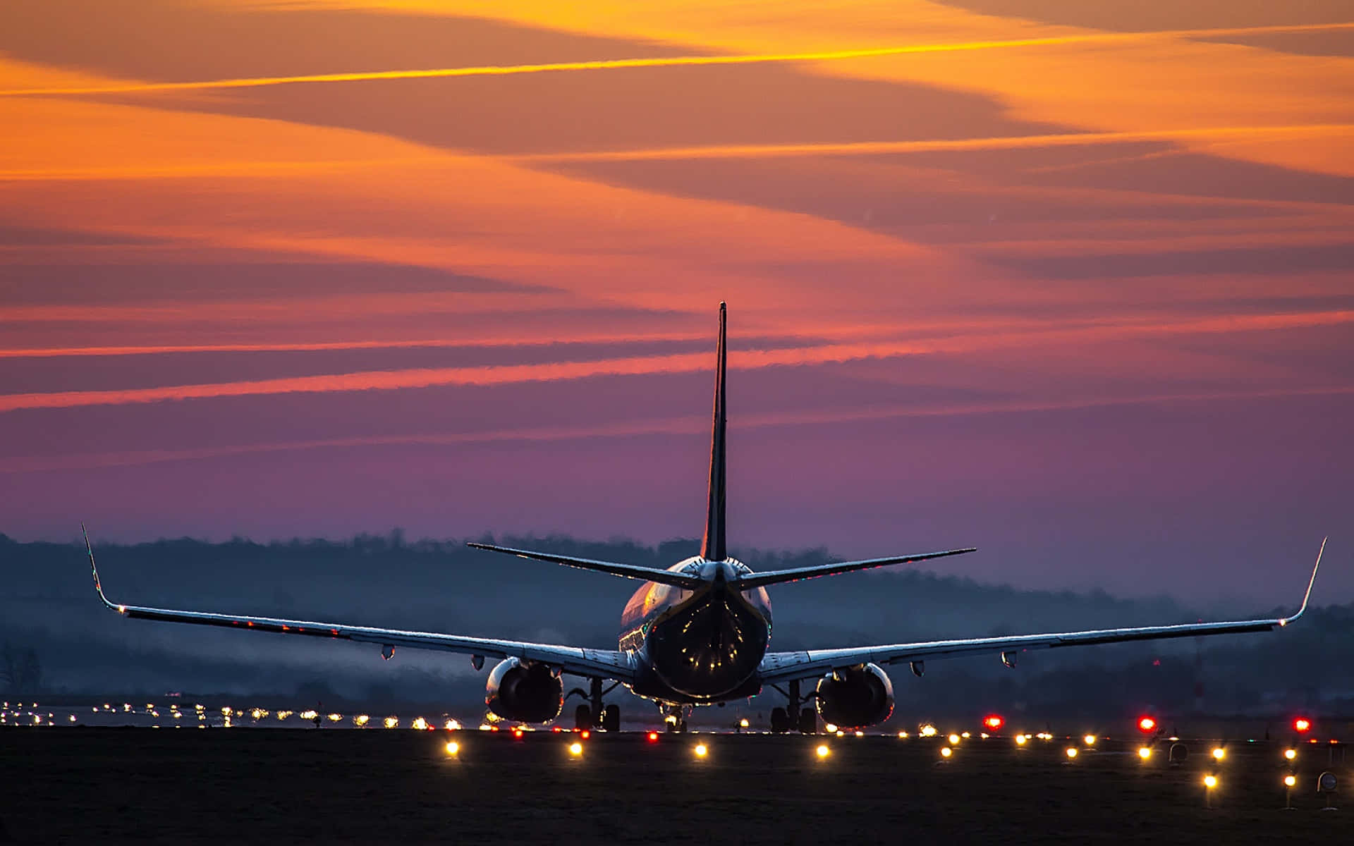 Flight 桌布 壁紙 — 一架商用飛機在跑道上以火熱的橙色和紫色日落為背景形成剪影。