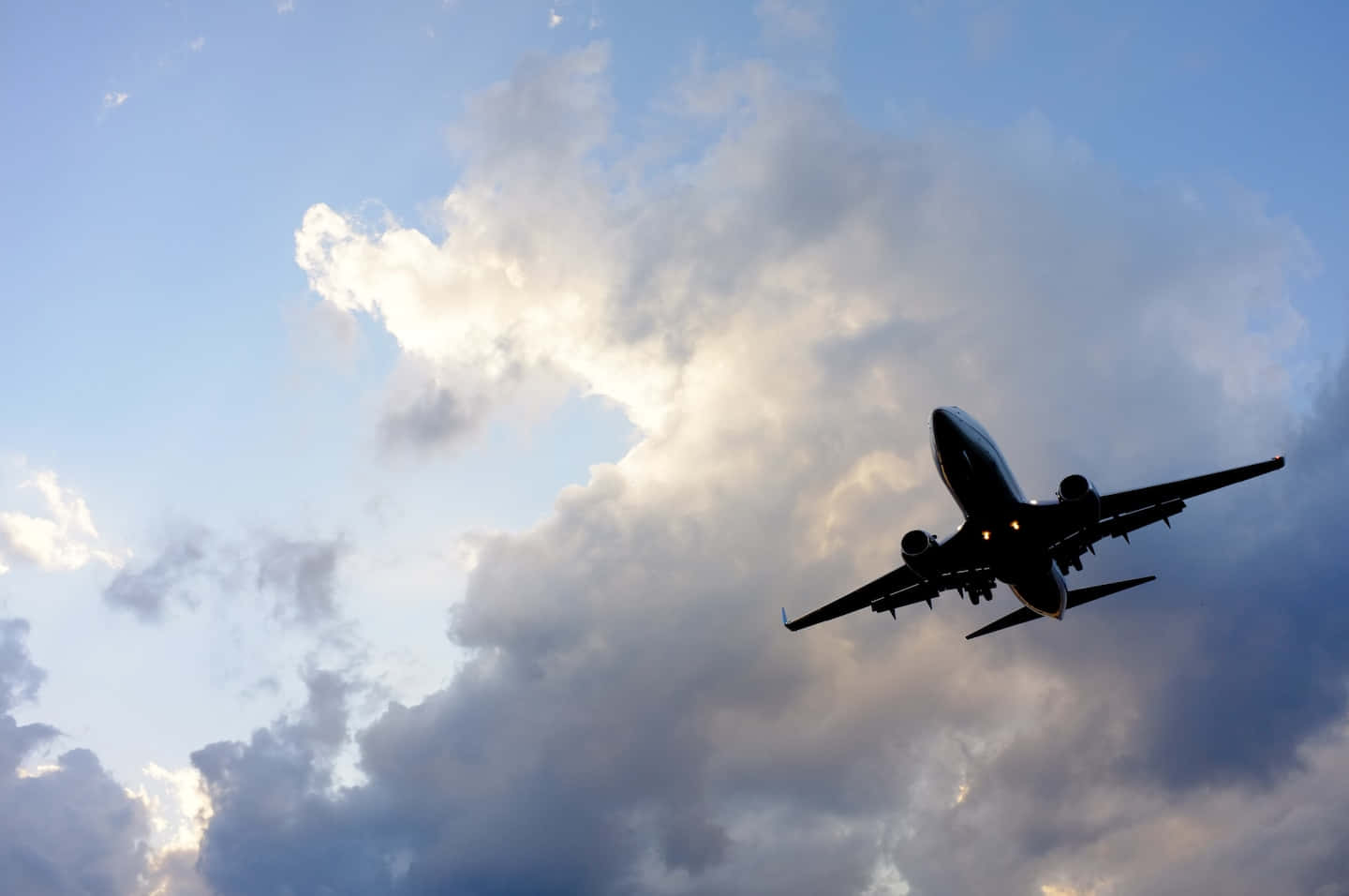 Aviation 桌布 壁紙 — 一架商用飛機在黃昏時分以戲劇性的天空和陽光照射的雲層為背景形成剪影。