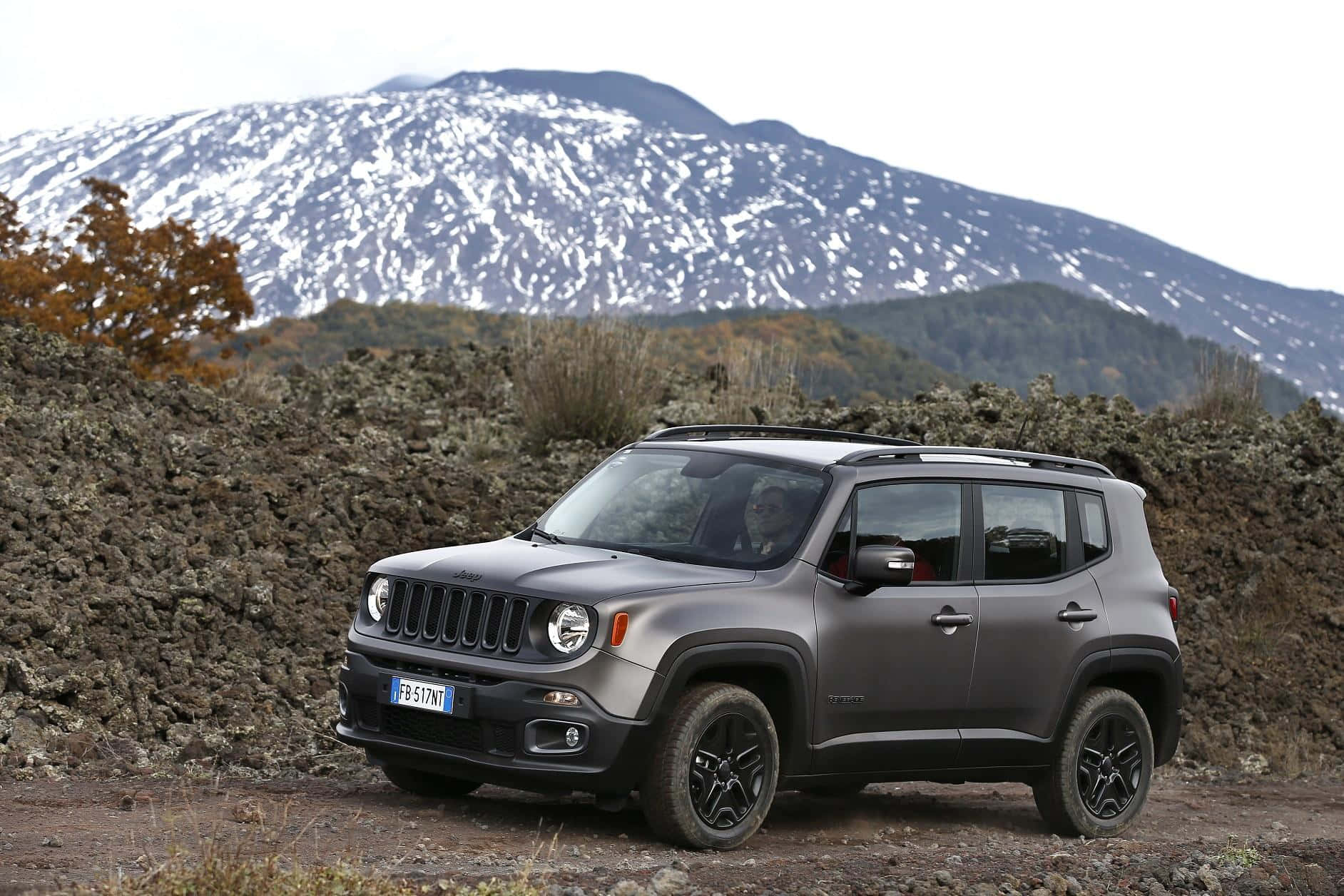 Jeep Renegade 桌布 壁紙 — 一架啞光灰色Jeep Renegade停泊喺崎嶇地形上，背景係一座被雪覆蓋嘅山。