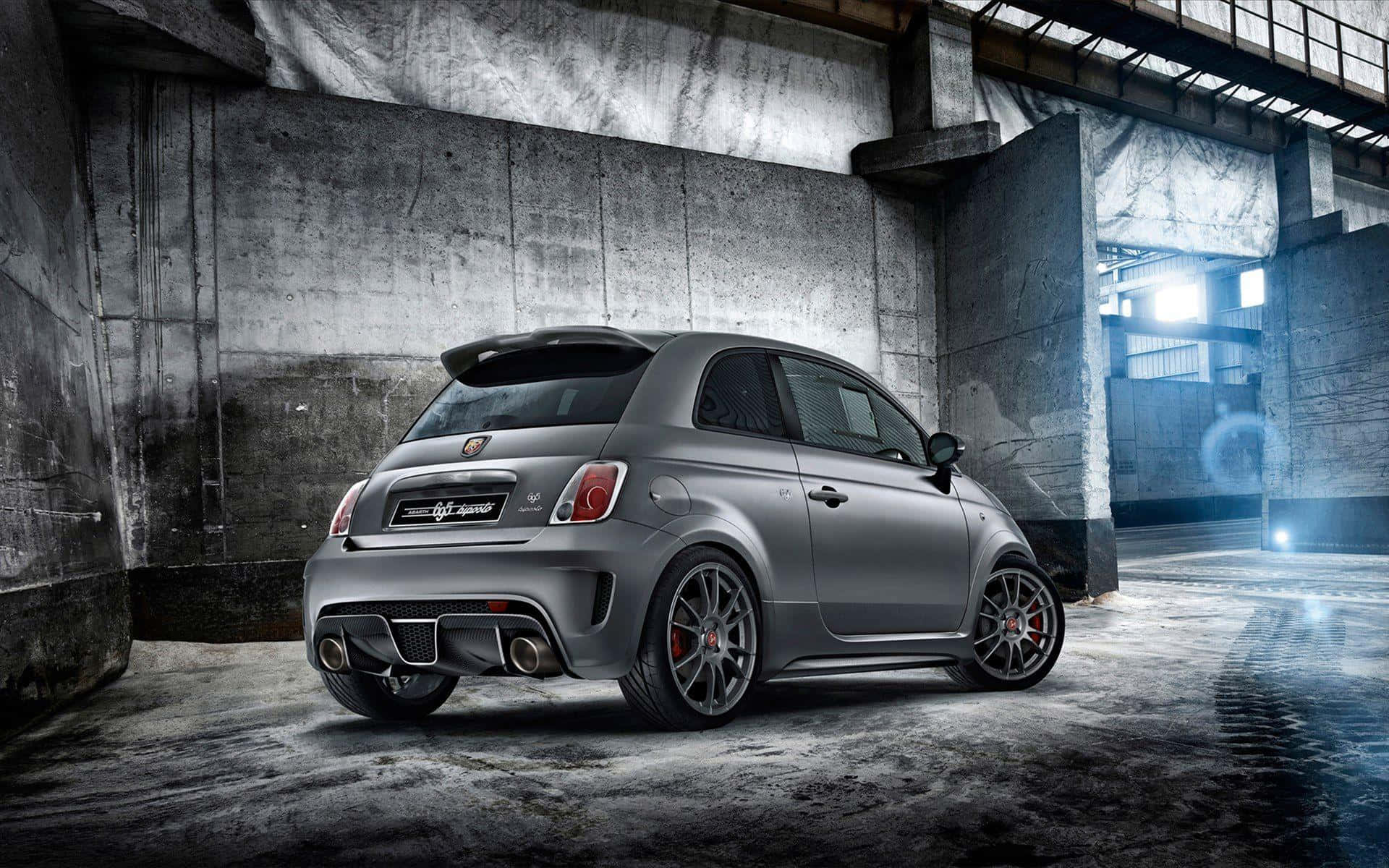 Abarth 桌布 壁紙 — 一架啞光灰色嘅Fiat 695 Abarth跑車停泊喺粗糙嘅混凝土倉庫入面，帶有戲劇性嘅燈光效果。
