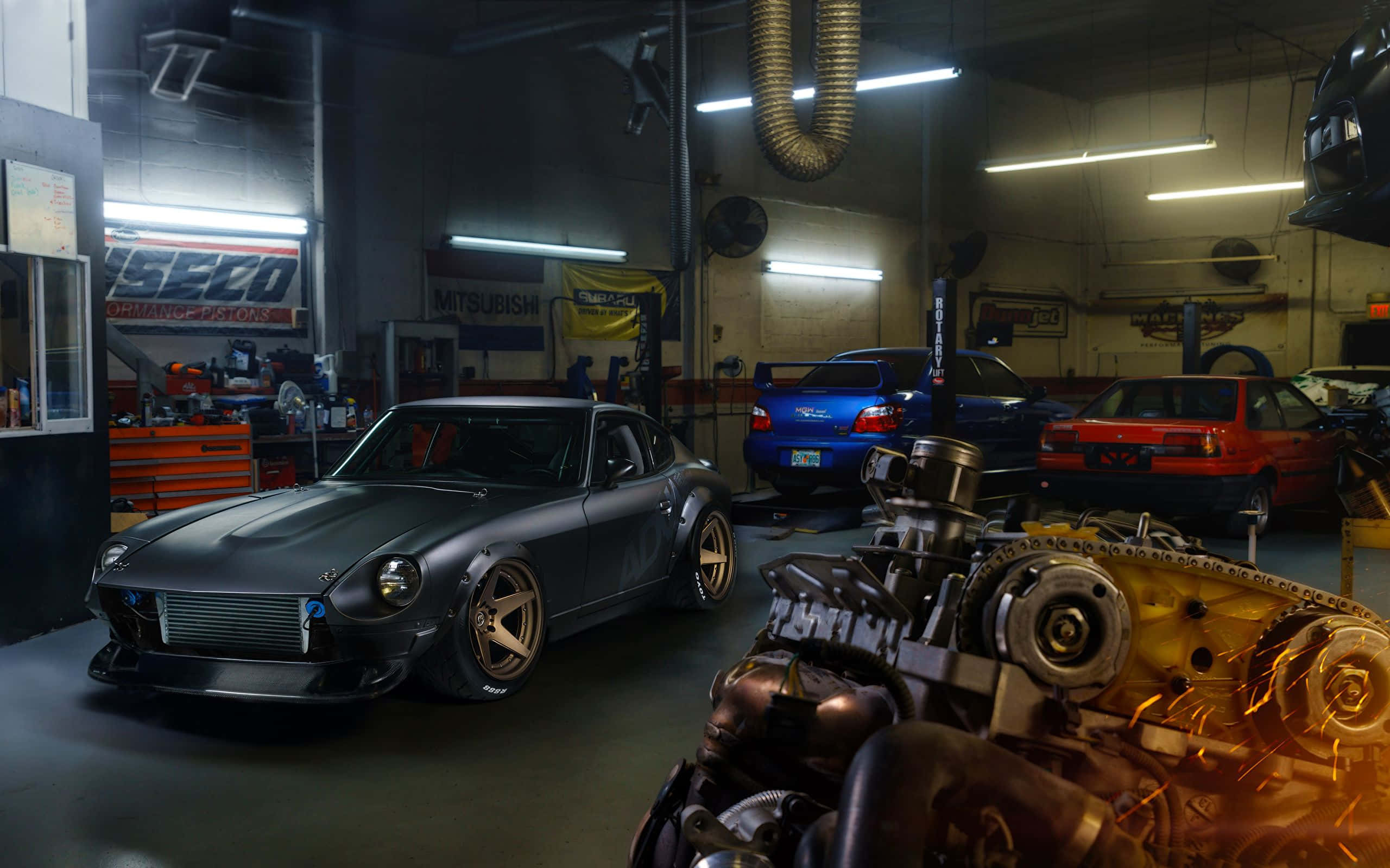 Garage 桌布 壁紙 — 一架啞光灰色改裝的Datsun 240Z停放在昏暗的車庫中，周圍有其他汽車和引擎零件，在螢光燈下。