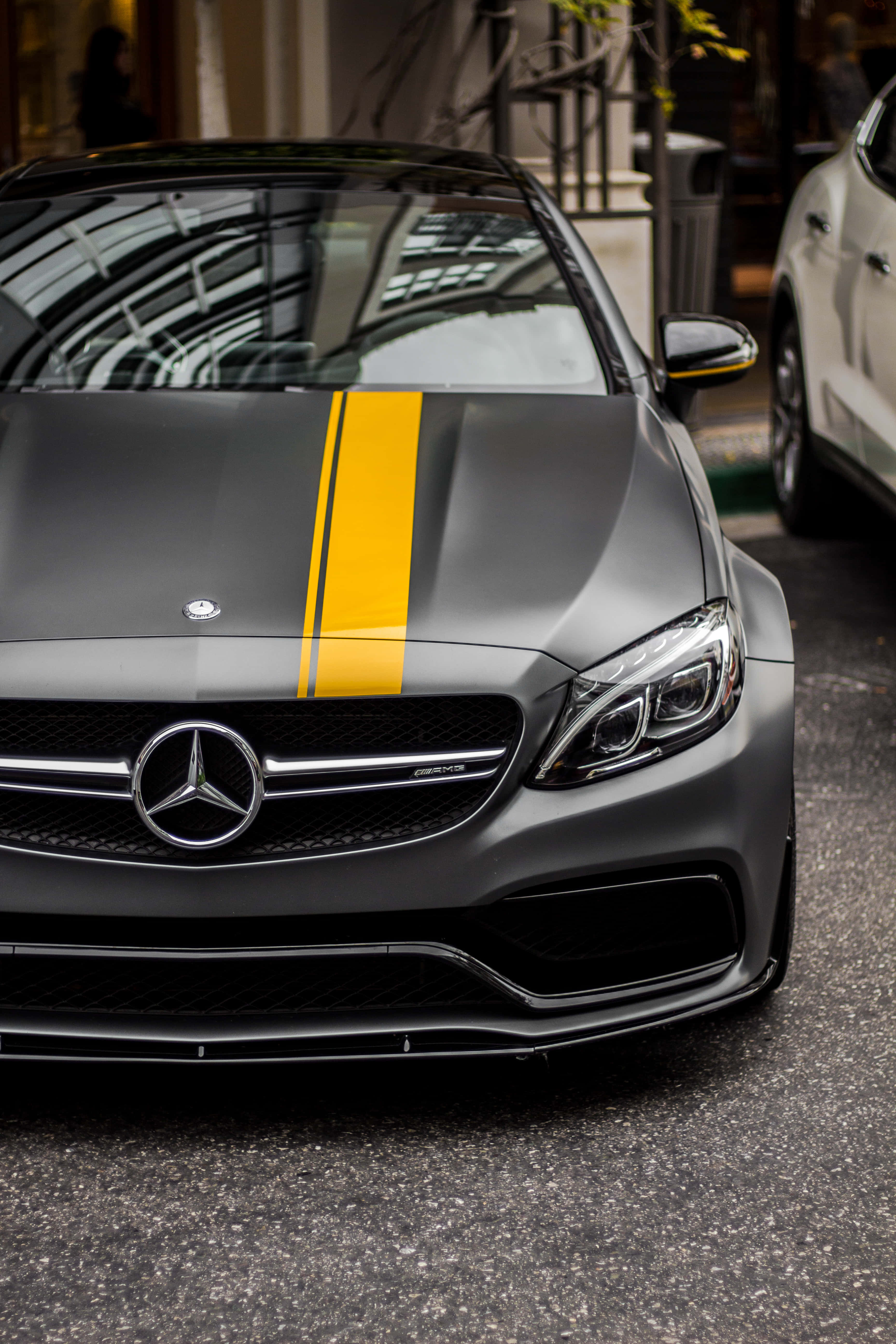 Best Car 桌布 壁紙 — 一架啞光灰色梅賽德斯-AMG跑車，帶有醒目的黃色條紋，停泊在城市街道上。