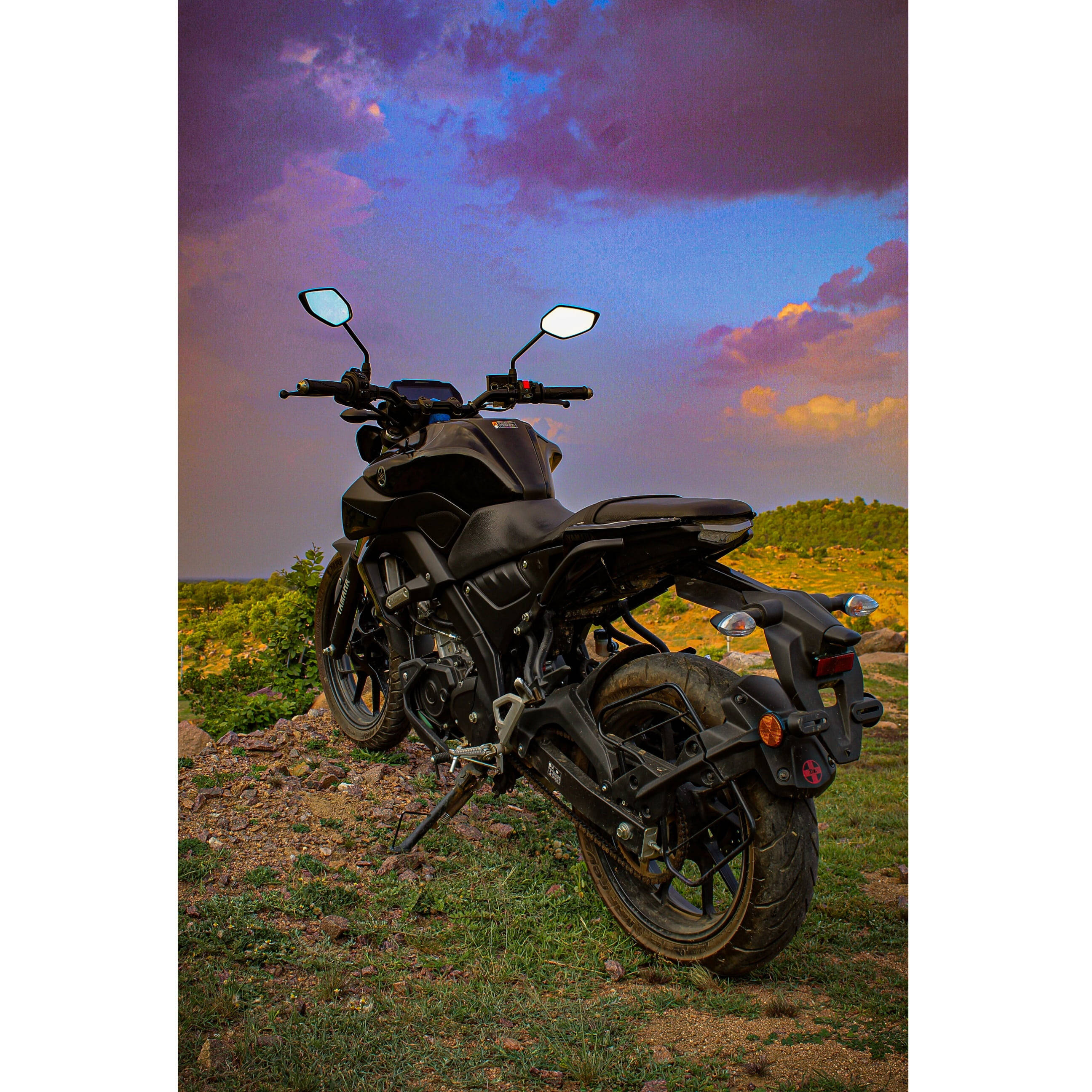 yamaha mt 15 桌布 壁紙 — 一架啞光黑色電單車停泊在草地上，背景是戲劇性的紫色和橙色日落天空。