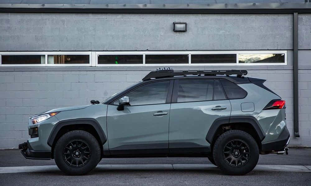 Family Car 桌布 壁紙 — 一架啞光鼠尾草綠色豐田RAV4，配黑色飾邊和車頂行李架，停在灰色磚砌建築前。