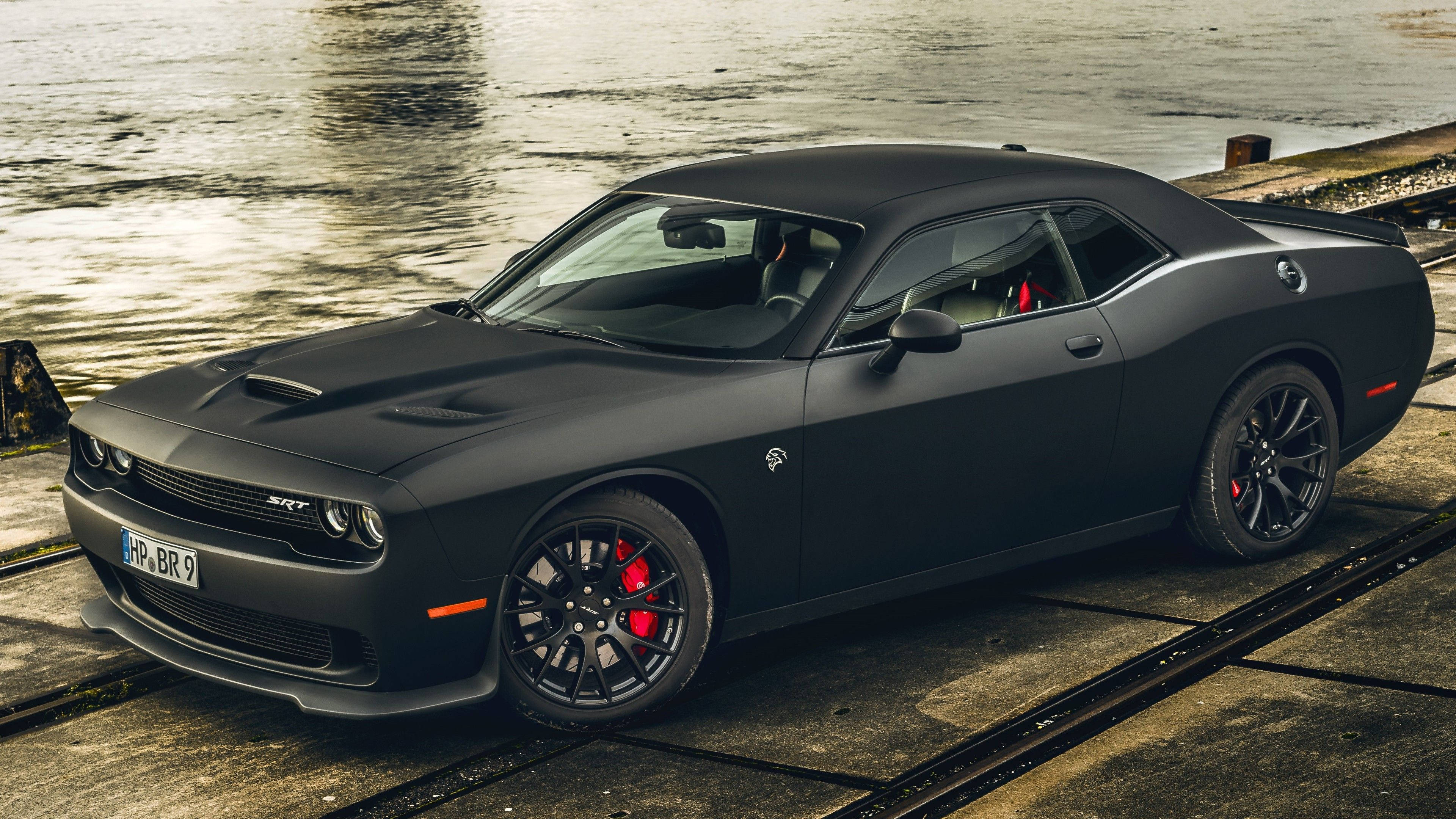 肌肉車 桌布 壁紙 — 一架啞黑色Dodge Challenger SRT停泊在近水的濕混凝土上，紅色制動卡鉗清晰可見。