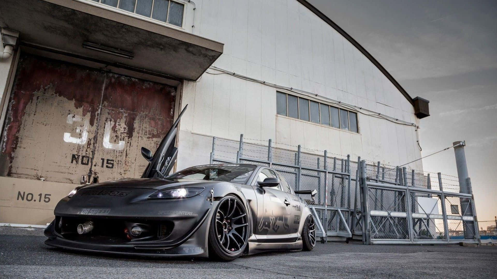 Mazda Rx-8 桌布 壁紙 — 一架啞黑色改裝跑車，打開鷗翼車門，停泊在黃昏時分風化的工業建築前。