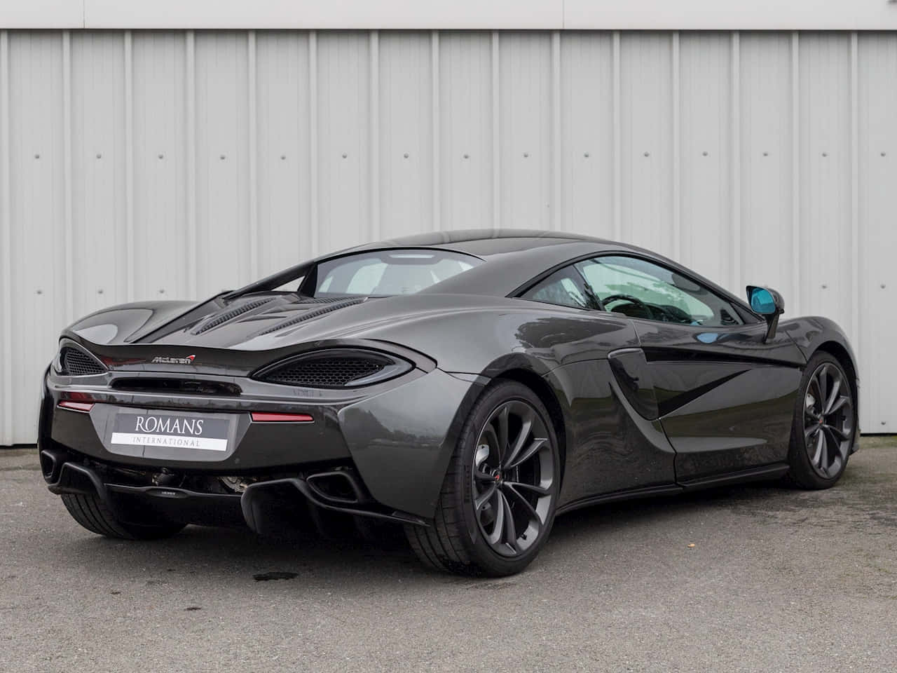 Mclaren 540c 桌布 壁紙 — 一架型格啞光灰色McLaren 600LT跑車停泊喺波浪形金屬牆旁邊，車牌寫住ROMANS INTERNATIONAL。