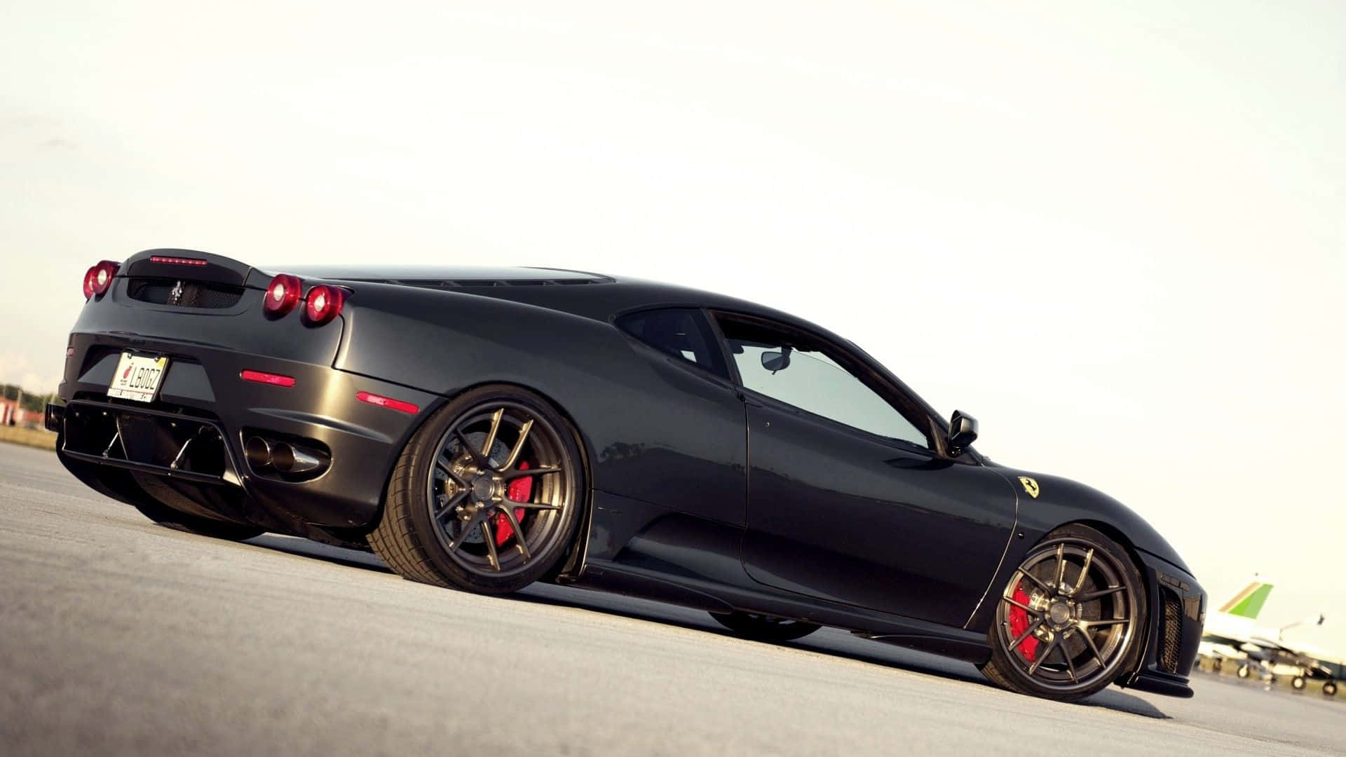 Ferrari F430 桌布 壁紙 — 一架型格啞黑色法拉利跑車，配備紅色制動卡鉗，在明亮日光下停泊在機場停機坪上。