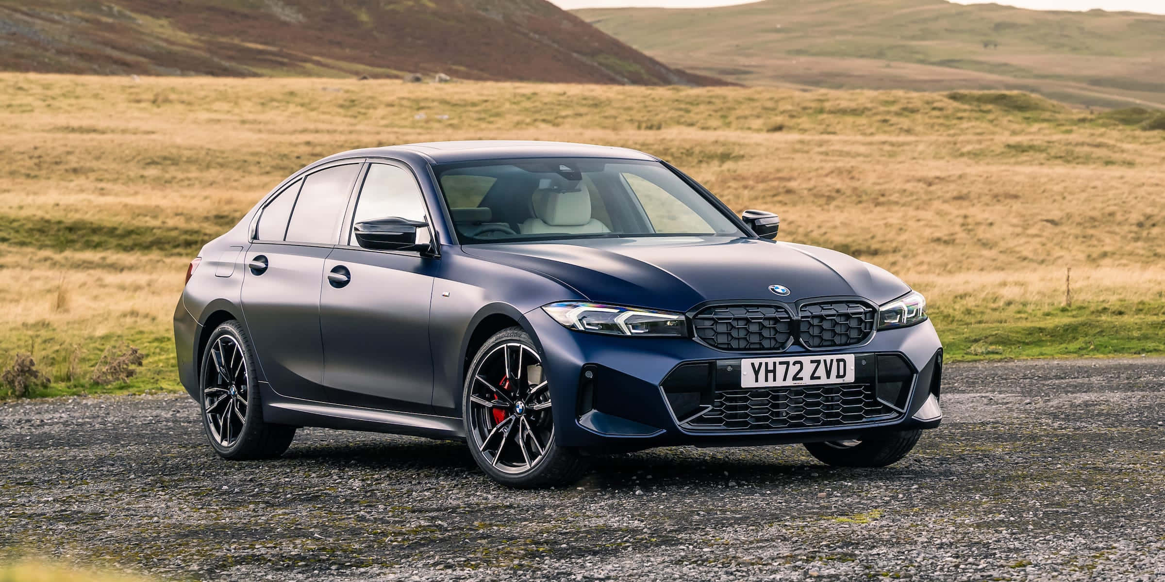 Bmw 3 Series 桌布 壁紙 — 一架型格嘅磨砂藍色寶馬3系房車停泊喺碎石路上，背景係起伏嘅金色山丘。