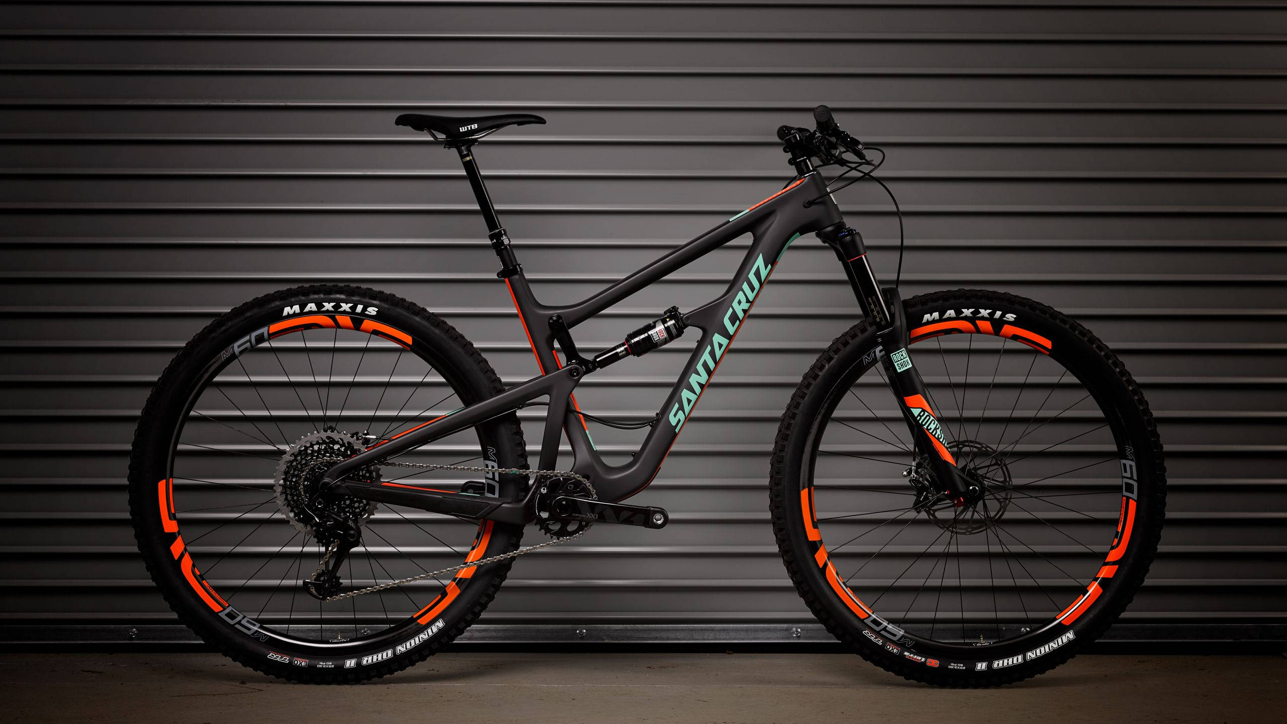Mountain Bike 桌布 壁紙 — 一架型格黑橙色Santa Cruz山地單車，矗立在深灰色波紋金屬背景前。