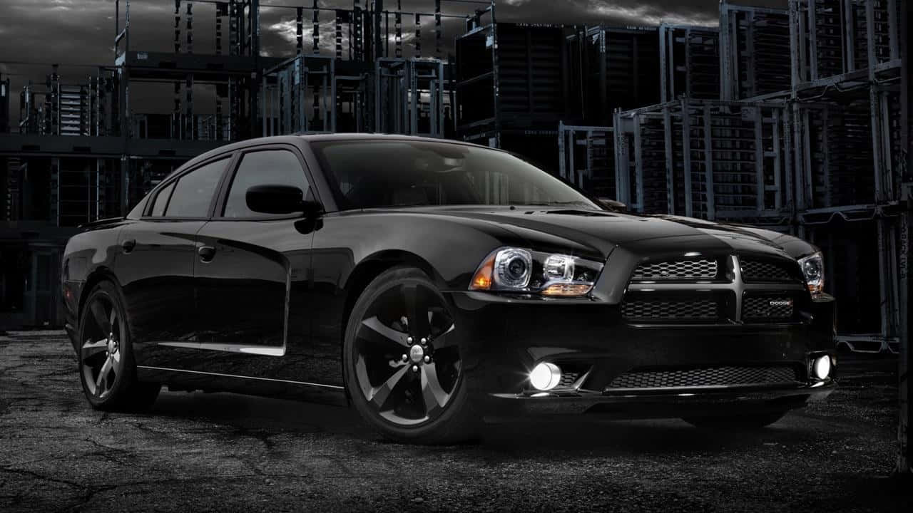 Dodge Charger 桌布 壁紙 — 一架型格黑色 Dodge Charger 停泊在風暴天空下嘅粗糙工業倉庫入面。