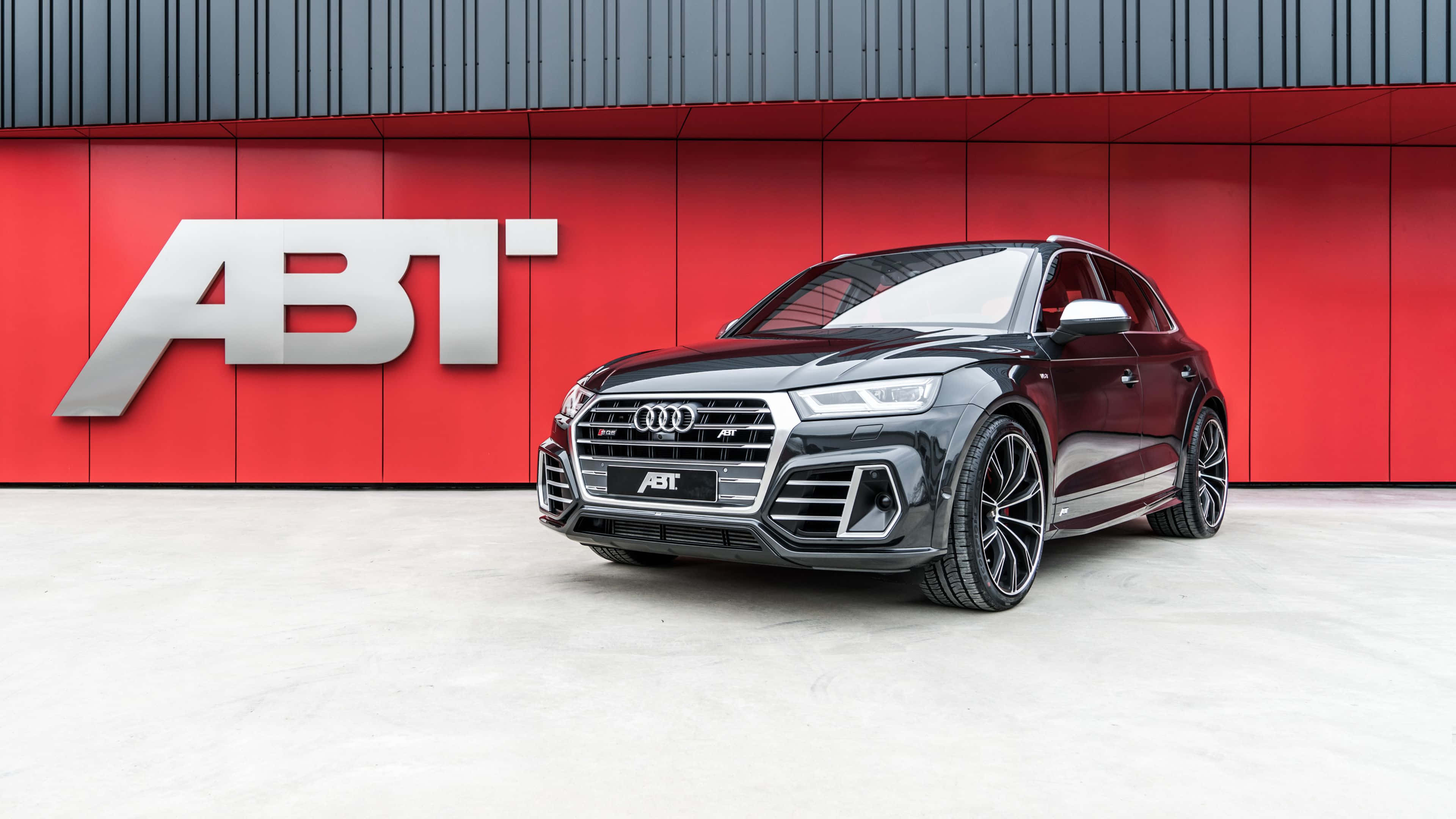 Audi Sq5 桌布 壁紙 — 一架型格黑色ABT改裝奧迪SQ5 SUV，停喺一面搶眼嘅紅色牆前面，牆上有銀色ABT標誌。
