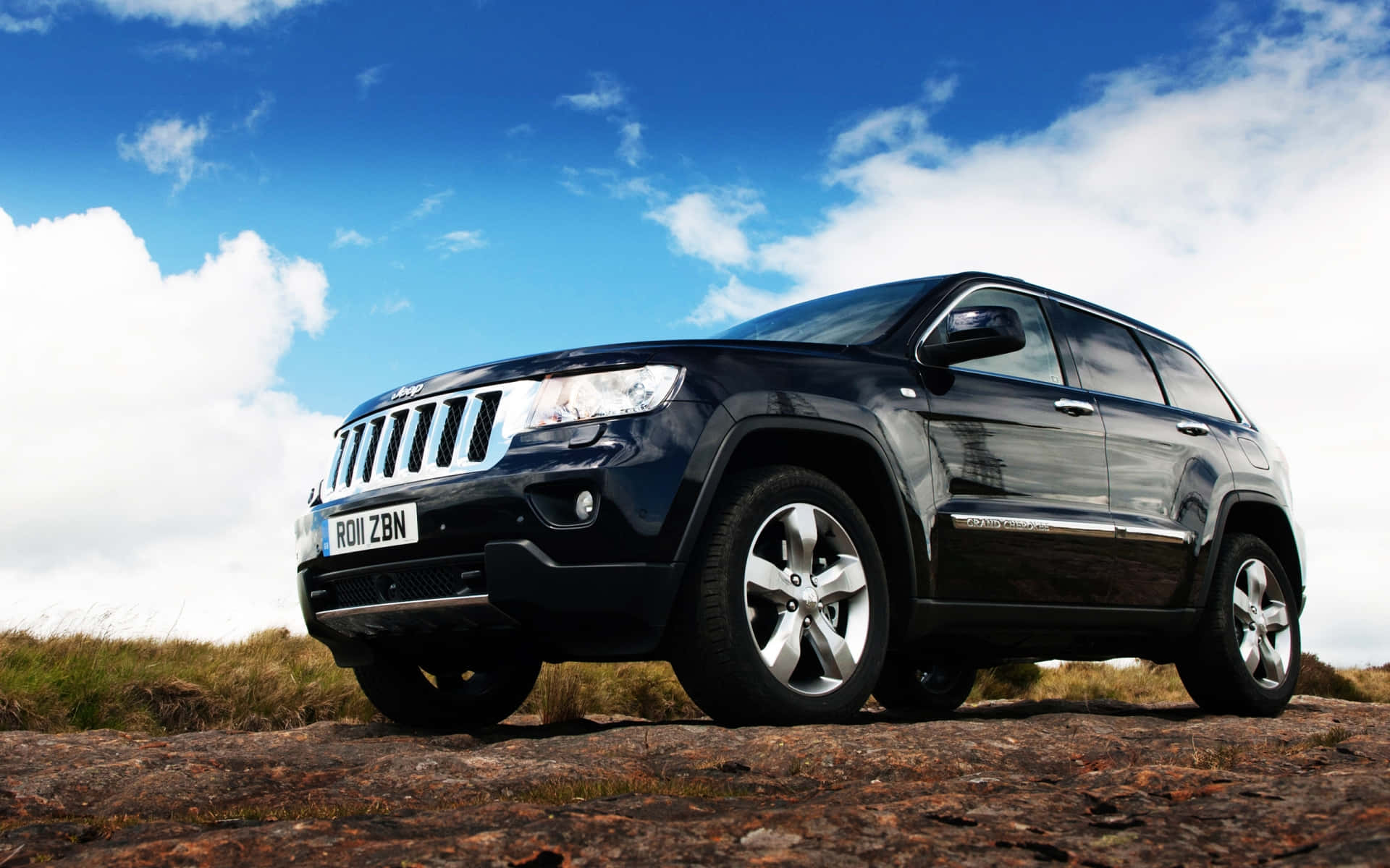 Ssangyong 桌布 壁紙 — 一架型格黑色Jeep Grand Cherokee喺藍天白雲下企喺堅固嘅岩石上。