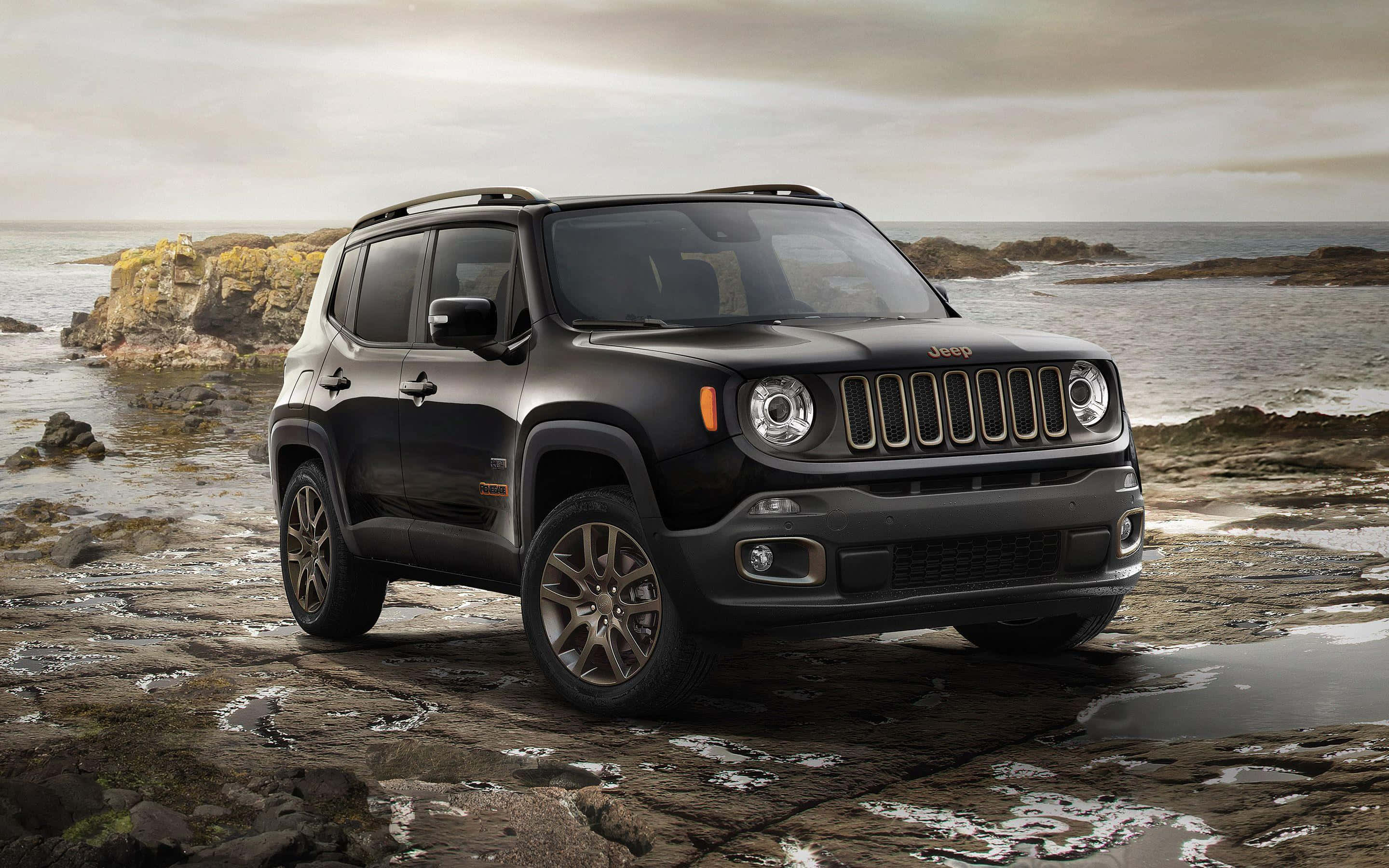 Jeep Renegade 桌布 壁紙 — 一架型格黑色Jeep Renegade停泊在濕漉漉的海岸岩石上，背後是洶湧的海浪和陰天。