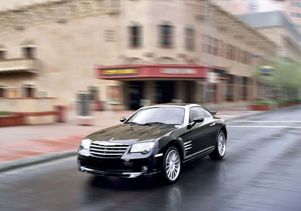 Chrysler Crossfire 桌布 壁紙 — 一架型格黑色克萊斯勒Crossfire在濕滑的城市街道上飛馳，建築物呈現動態模糊，路面有倒影。