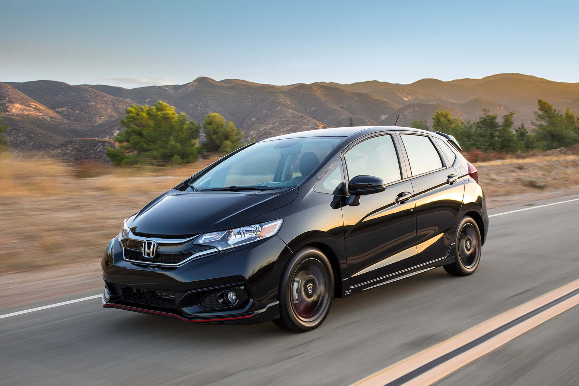 Honda Fit 桌布 壁紙 — 一架型格黑色本田Fit喺沙漠公路高速飛馳，背景係陽光普照嘅山脈同稀疏嘅綠植，呈現動態模糊效果。