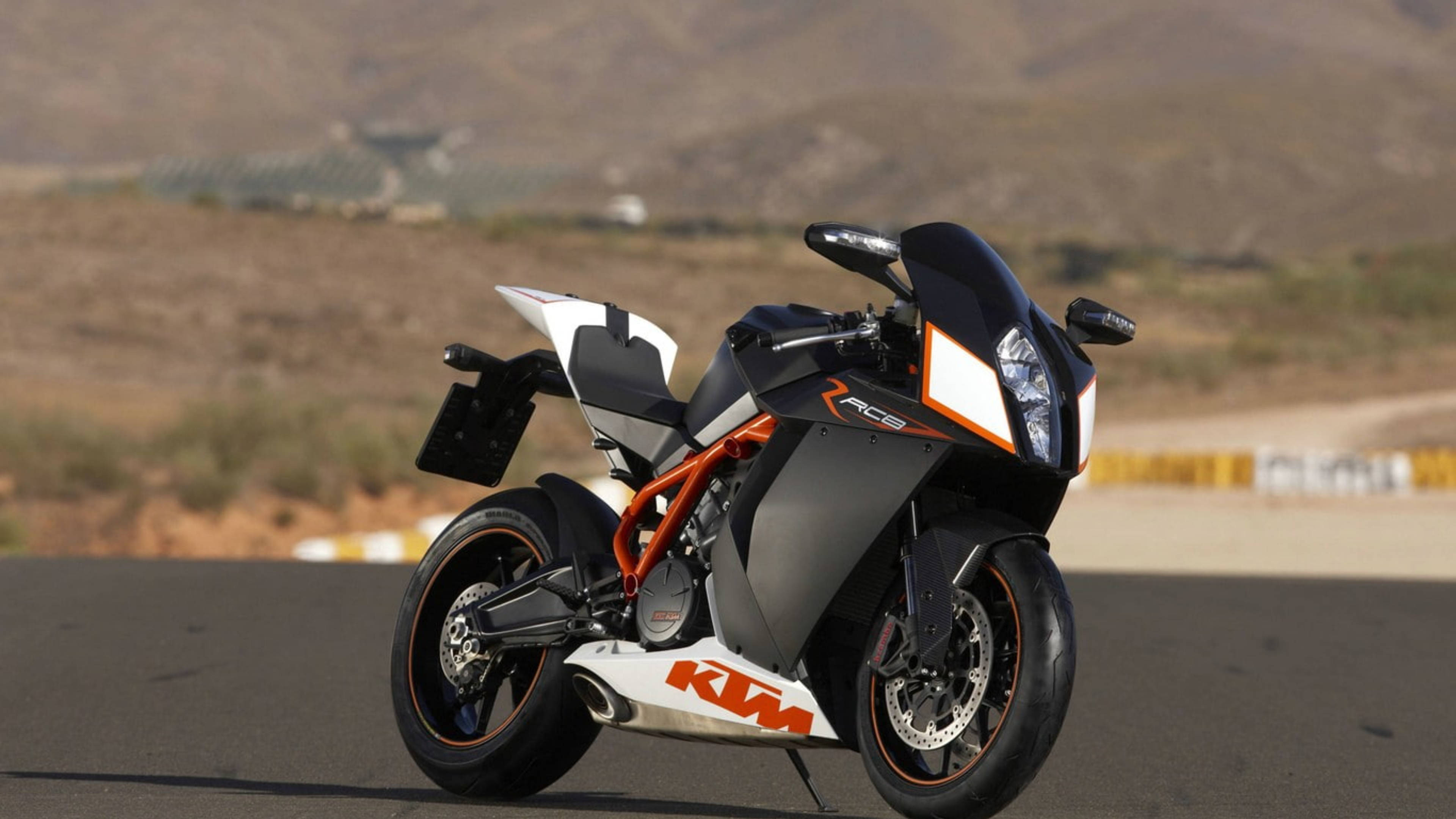 機車 桌布 壁紙 — 一架型格黑色橙色KTM RC8跑車電單車停泊在瀝青賽道上，背景是乾旱的山丘。