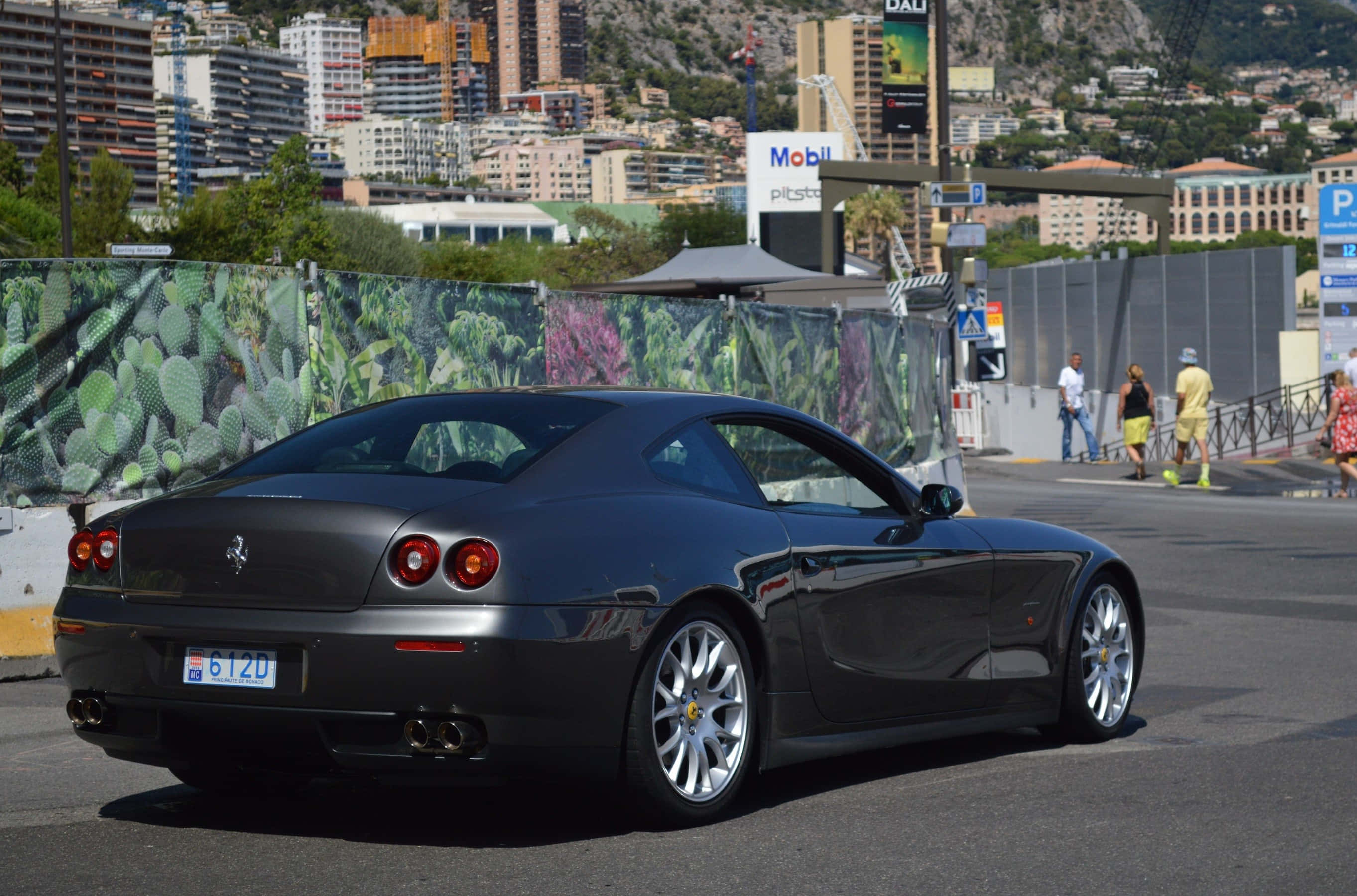 Ferrari 612 Scaglietti 桌布 壁紙 — 一架型格黑色法拉利跑車停泊在陽光明媚的城市街道上，背景是城市天際線和仙人掌圍欄。