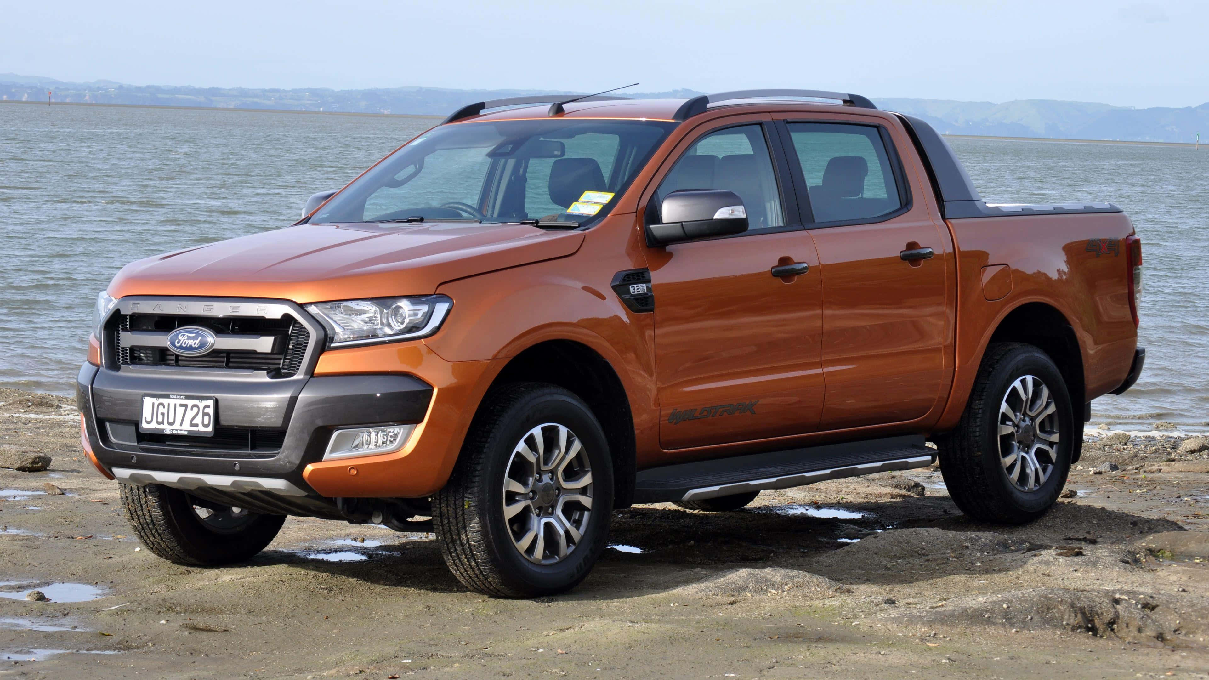 Ford Ranger 桌布 壁紙 — 一架堅固的橙色福特 Ranger  pickup 貨車停泊在泥濘的岸邊，平靜的水面和遠處的山丘在朦朧的天空下。