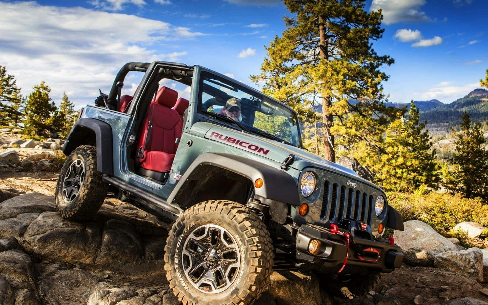 Jeep Cj 桌布 壁紙 — 一架堅固的綠色Jeep Rubicon配紅色座椅，在點綴著白雲的明亮藍天下攀爬岩石地形。