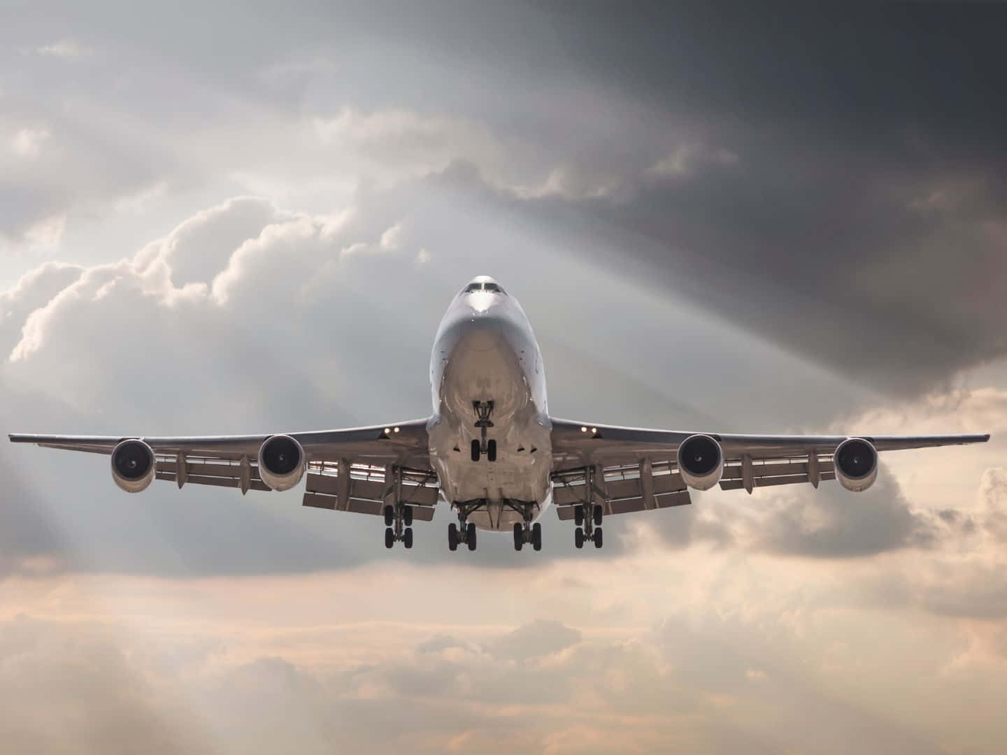 從下方觀看一架大型客機穿過雲層下降，陽光穿透雲層。
