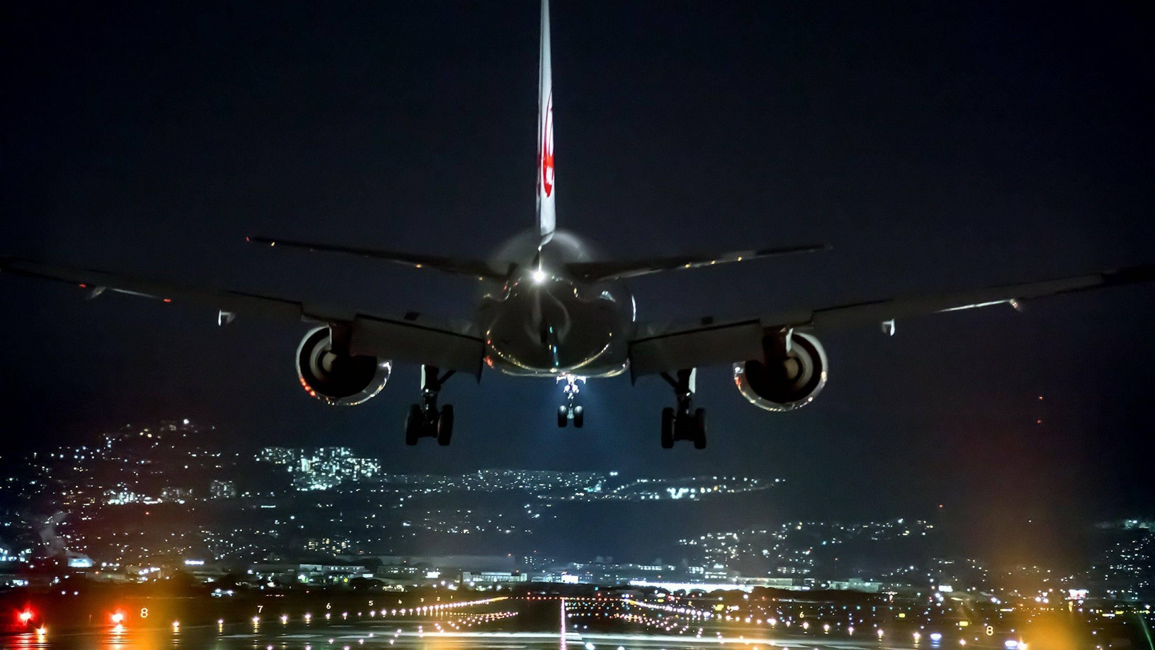 飛機 桌布 壁紙 — 一架大型飛機在夜間下降，降落燈亮著，下方是燈火通明的城市景觀。