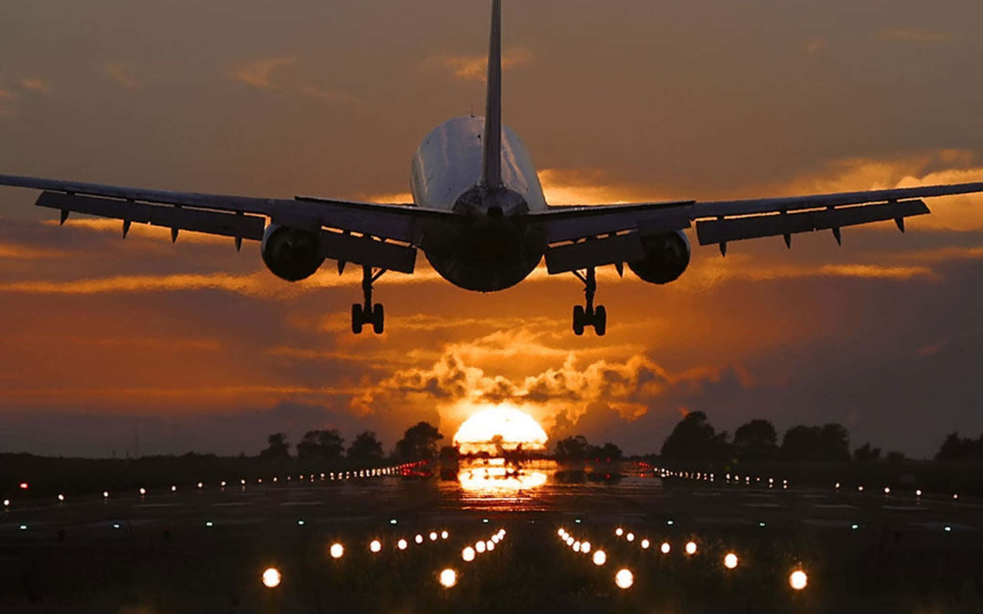 Flight 桌布 壁紙 — 一架大型飛機正下降至跑道，太陽在其後方落下，將金色光芒灑在雲層和跑道燈上。