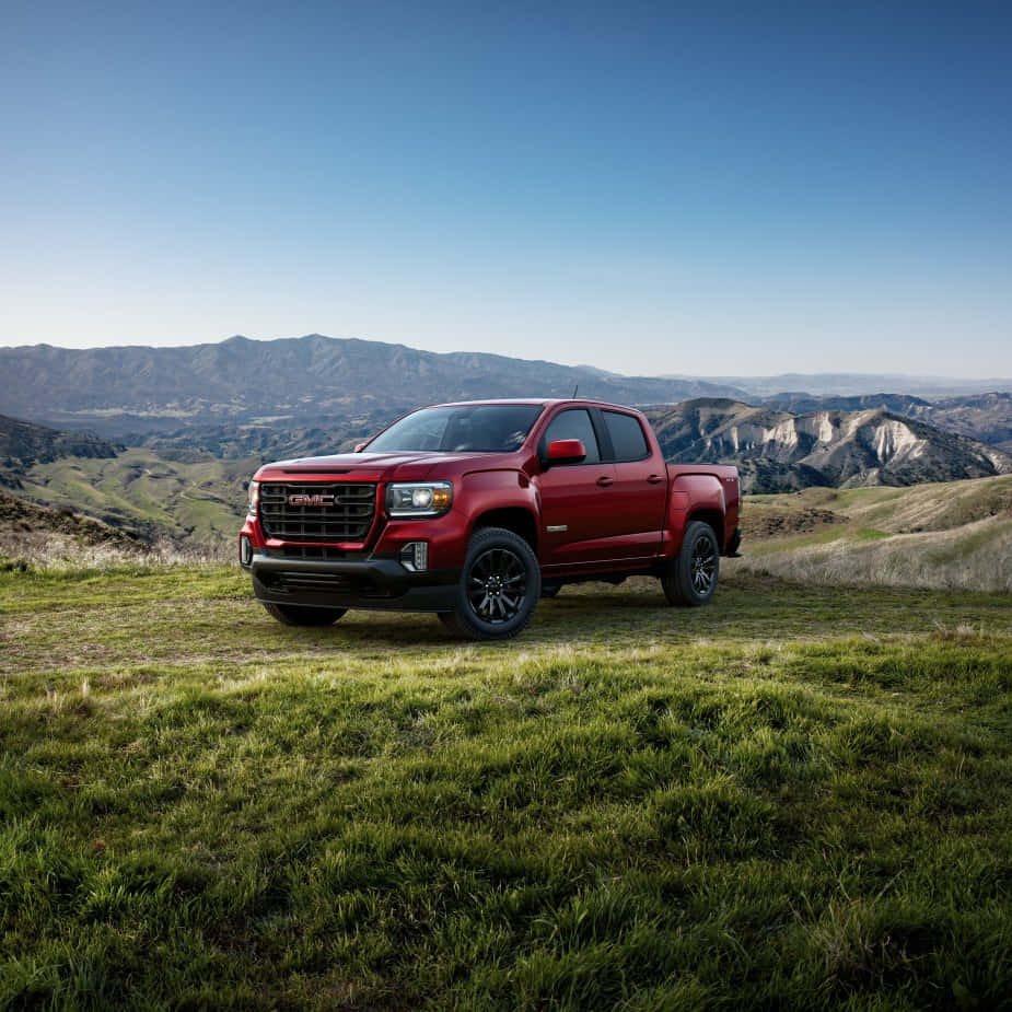Gmc Canyon 桌布 壁紙 — 一架大膽的紅色GMC Sierra皮卡車停泊在陽光明媚的草地上，俯瞰著連綿起伏的山脈，天空湛藍清澈。