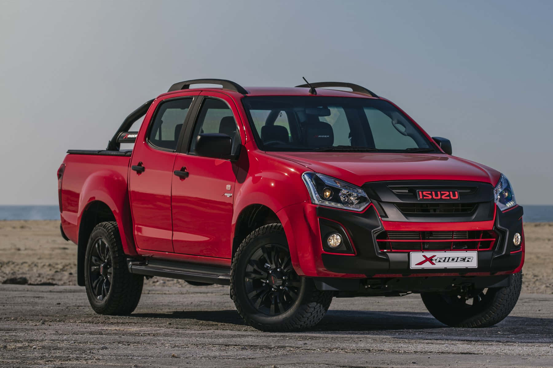 Isuzu 桌布 壁紙 — 一架大膽的紅色Isuzu X-Rider pickup貨車停泊在陽光明媚的海灘上，背後是海洋地平線。